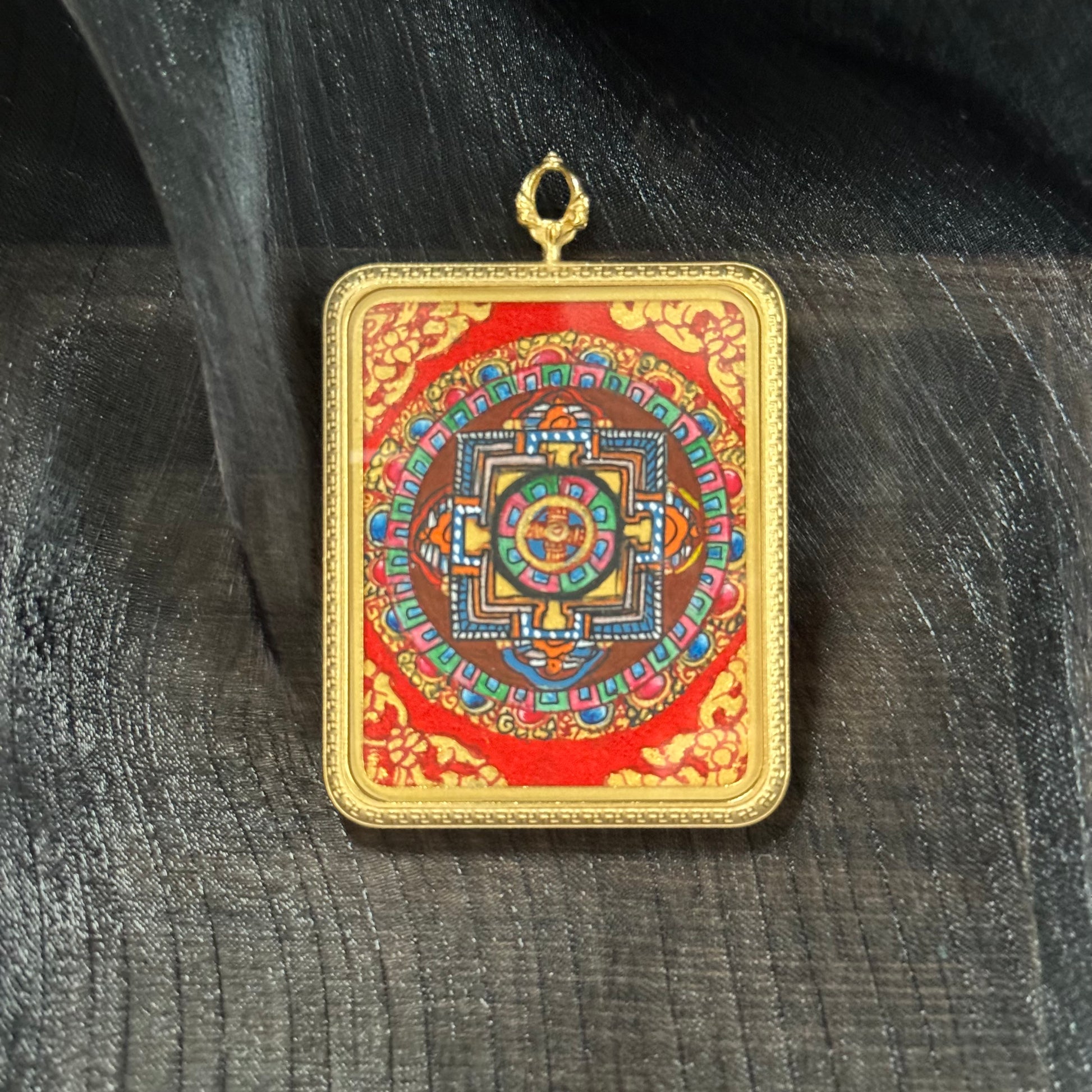 Hand-painted Nepal mandala mini thangka pendant featuring a detailed sacred geometry mandala with traditional mineral pigments on a red background, set in a square gold-tone frame with hanging loop.