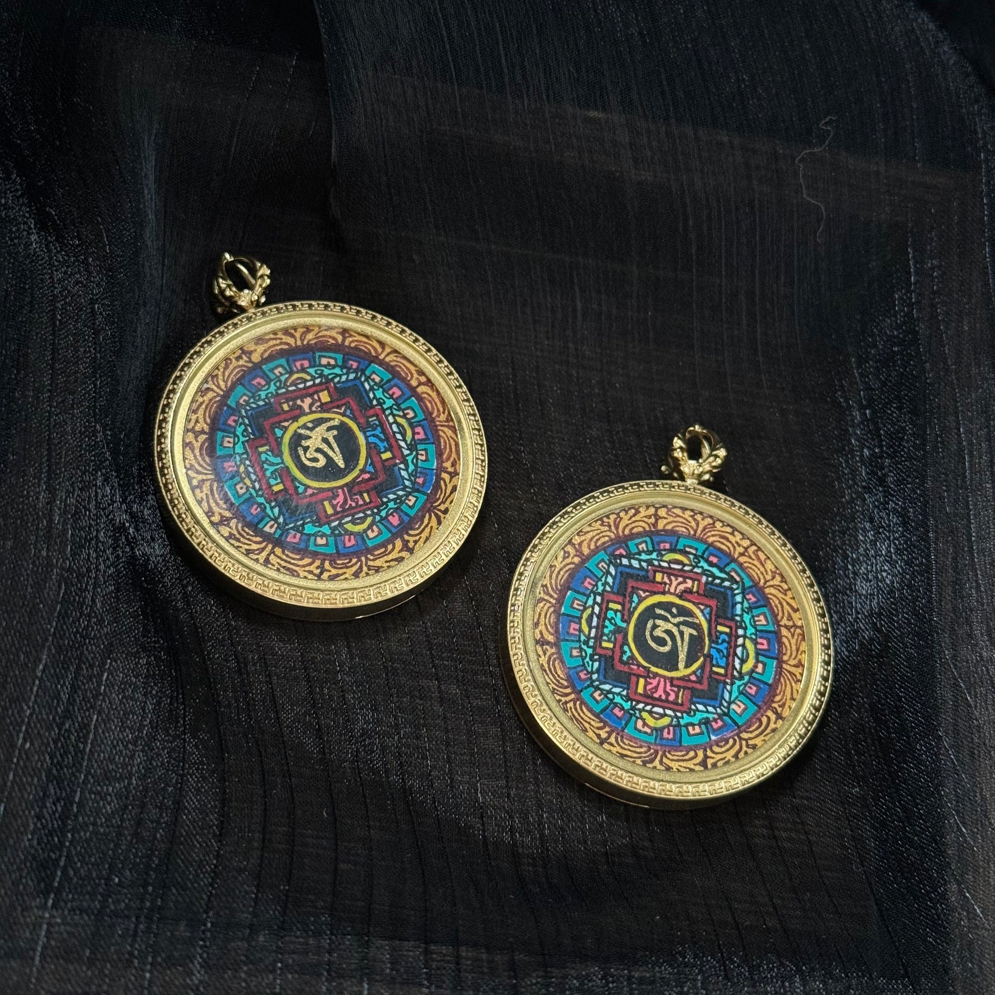 Two Nepal mandala miniature thangka pendants displayed on dark fabric background showing symmetrical Buddhist mandala patterns and hand-painted details