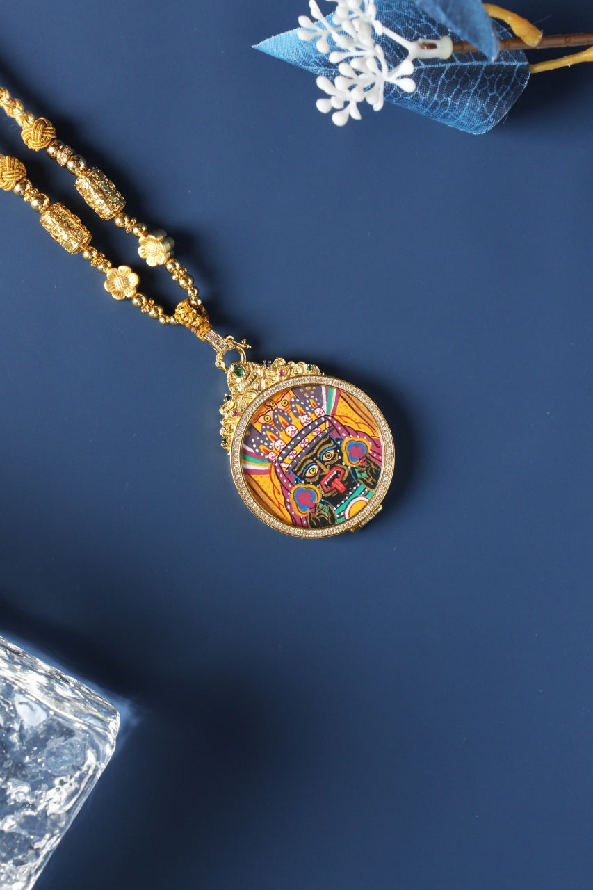 Angled view of Zaki Lhamo mini thangka pendant showing round pendant structure, layered mineral pigments, and decorative metal frame details
