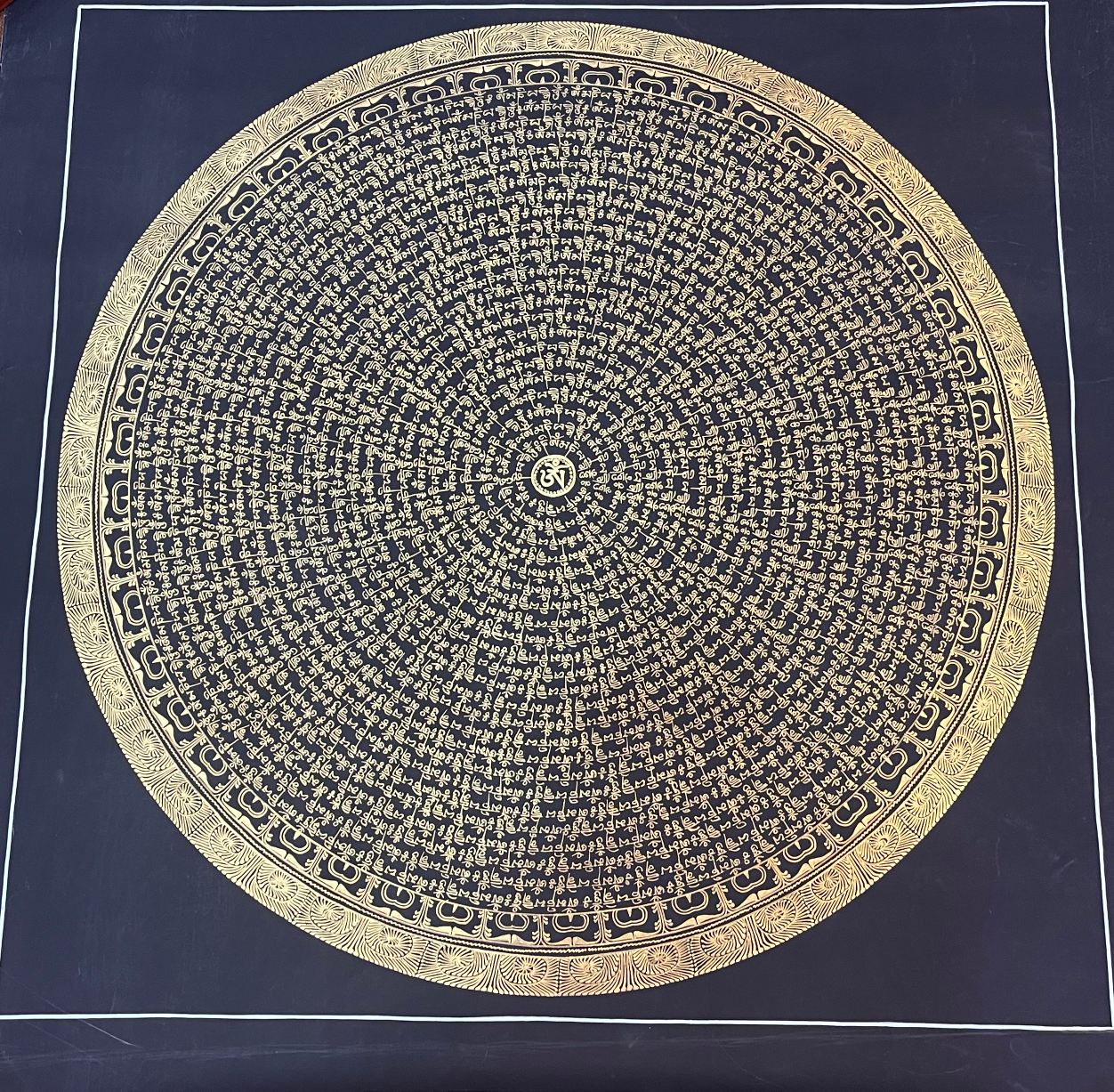 Large black and gold thangka featuring the Om Mani Padme Hum mantra arranged in concentric circular script, hand-painted with gold calligraphy on dark canvas in the Nepal thangka tradition.