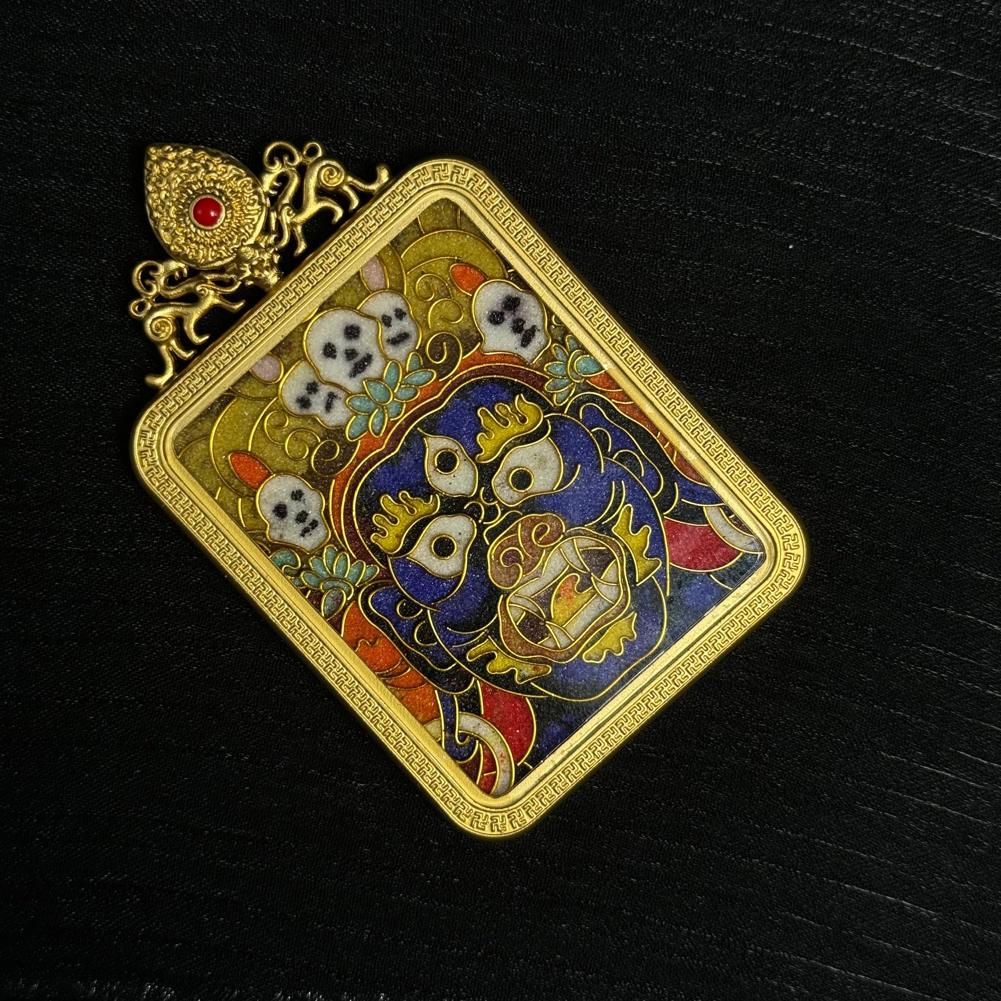 Close-up detail of a Palden Lhamo mini thangka pendant featuring the colorful wrathful face motif, skull ornaments, cloisonné enamel craftsmanship, and 24K gold-plated border.