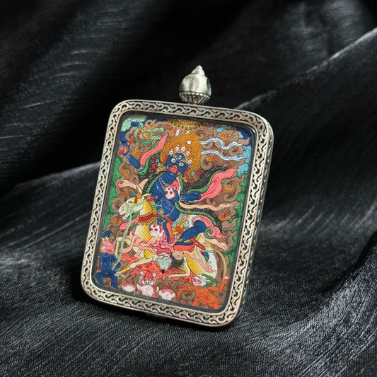 Angled view of a Palden Lhamo Tibetan mini thangka pendant showing detailed deity painting, mineral pigment colors, and ornamental metal frame.