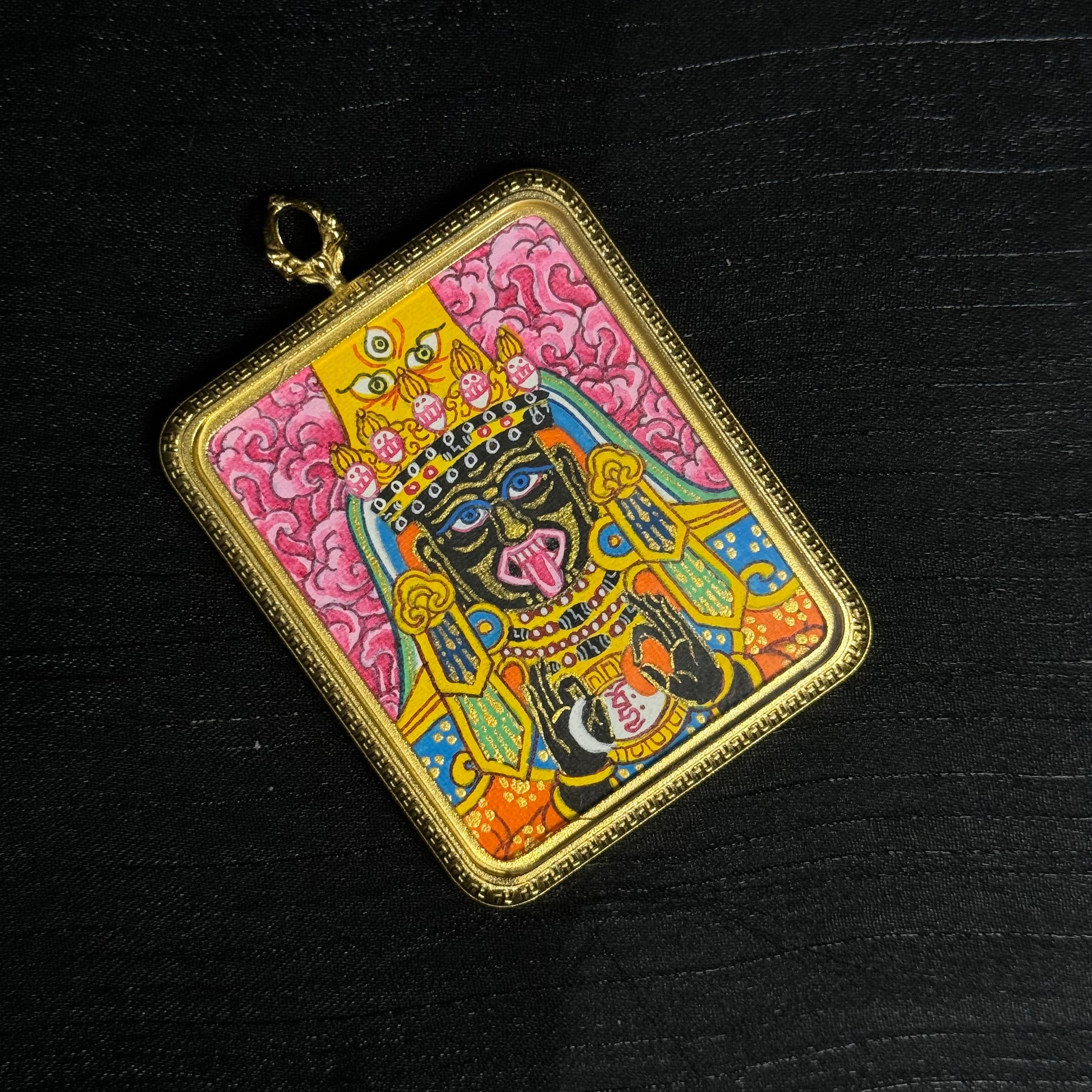 Flat lay view of pink Zaki Lhamo mini thangka pendant showing intricate hand painted deity portrait, vibrant mineral pigment colors and decorative square metal frame used for portable Tibetan Buddhist art.