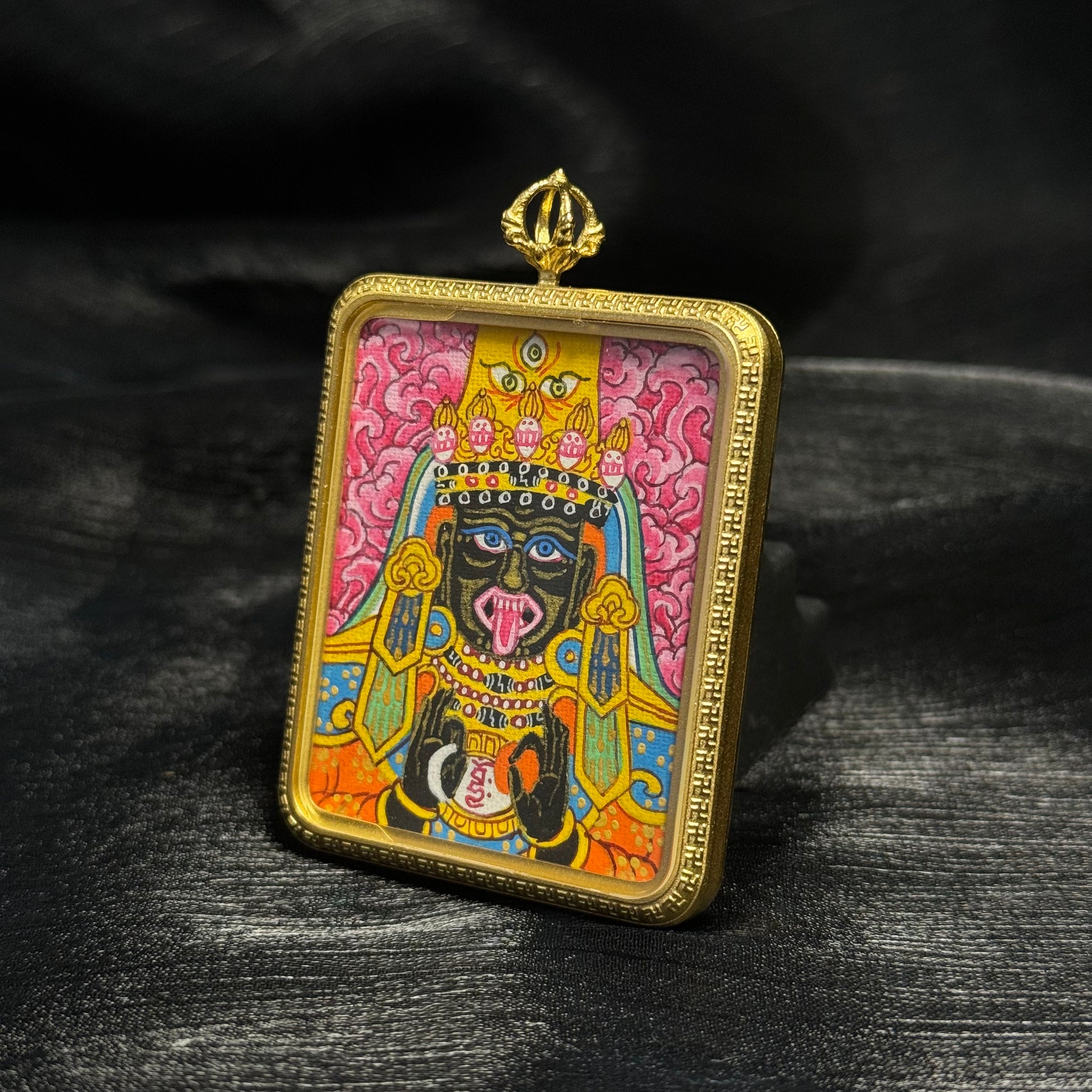 Three quarter perspective of Nepalese hand painted Zaki Lhamo mini thangka pendant featuring pink background clouds, expressive deity features, colorful robes and traditional miniature thangka painting details.
