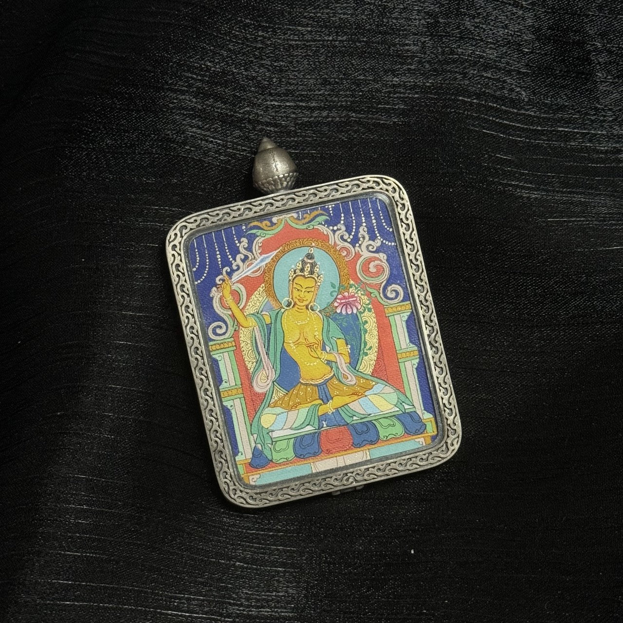 Manjushri Bodhisattva thangka painting in Qigang style showing seated wisdom bodhisattva holding flaming sword and lotus within decorative silver pendant frame