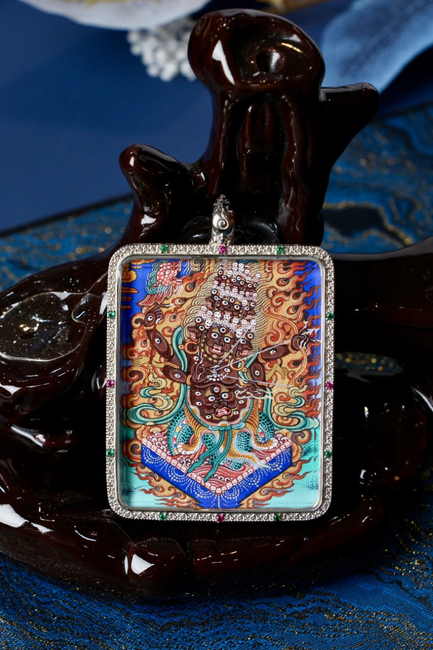 Close-up of the Rahu (Rahula) wrathful protector thangka painting inside a 925 silver Gawu pendant, photographed on a dark display stand with blue textile background.
