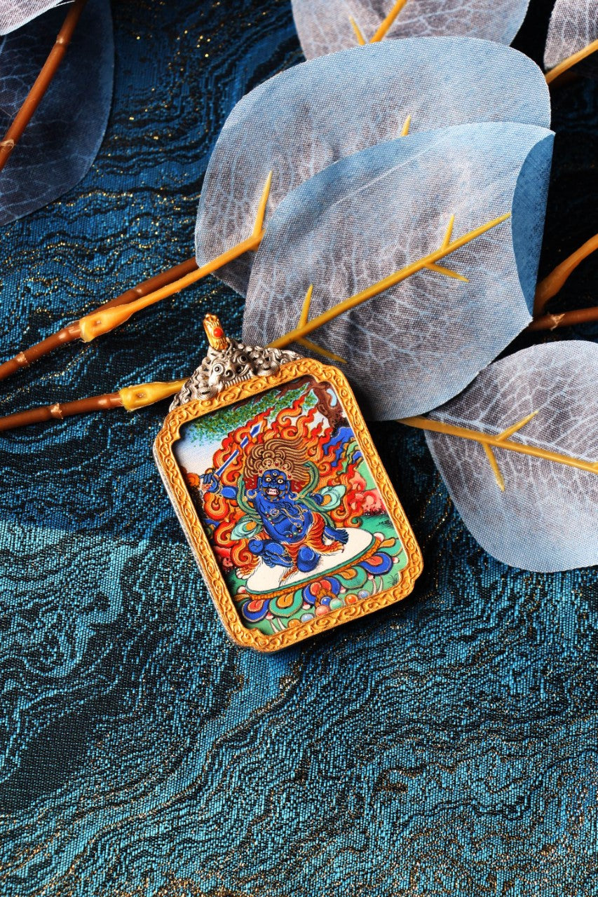 Angled display of Rebgong Acala Thangka pendant showing dynamic wrathful deity form, fine linework, layered mineral colors, and silver-plated frame