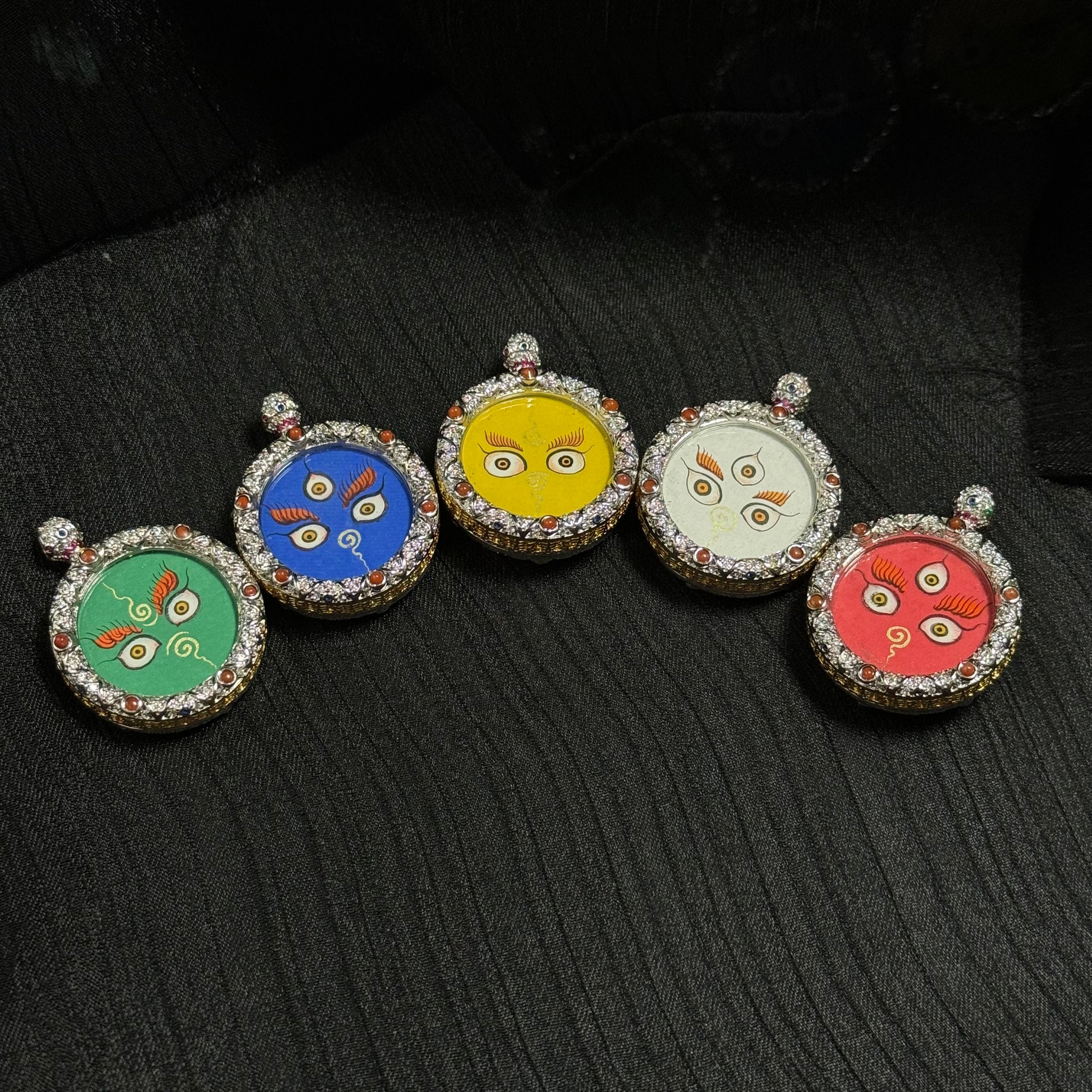 Five Jambhala wealth eye miniature thangka pendants arranged side by side, featuring hand-painted sacred eyes on colored backgrounds representing the five elemental wealth deities.