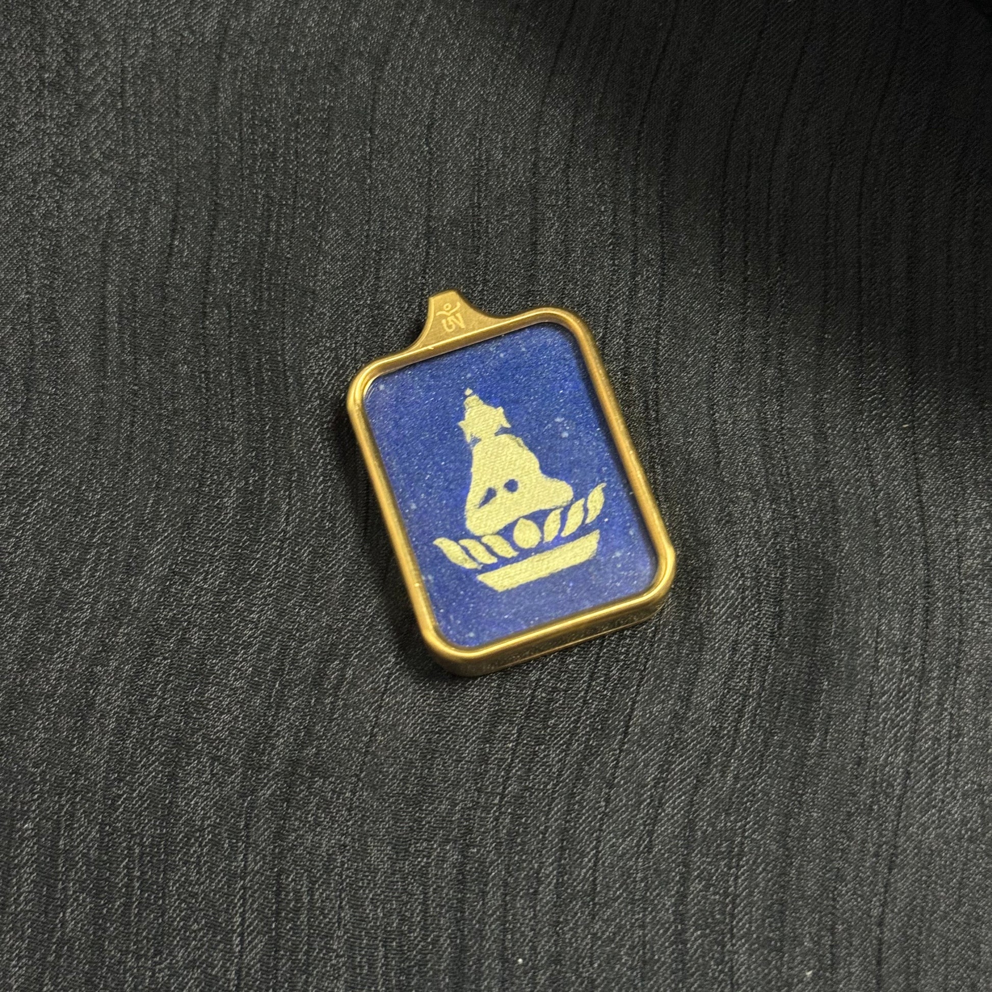 Angle view of a Rebgong hand-painted Formless Buddha mini thangka pendant showing the gold Buddha silhouette seated on a lotus against a shimmering lapis lazuli mineral pigment background.