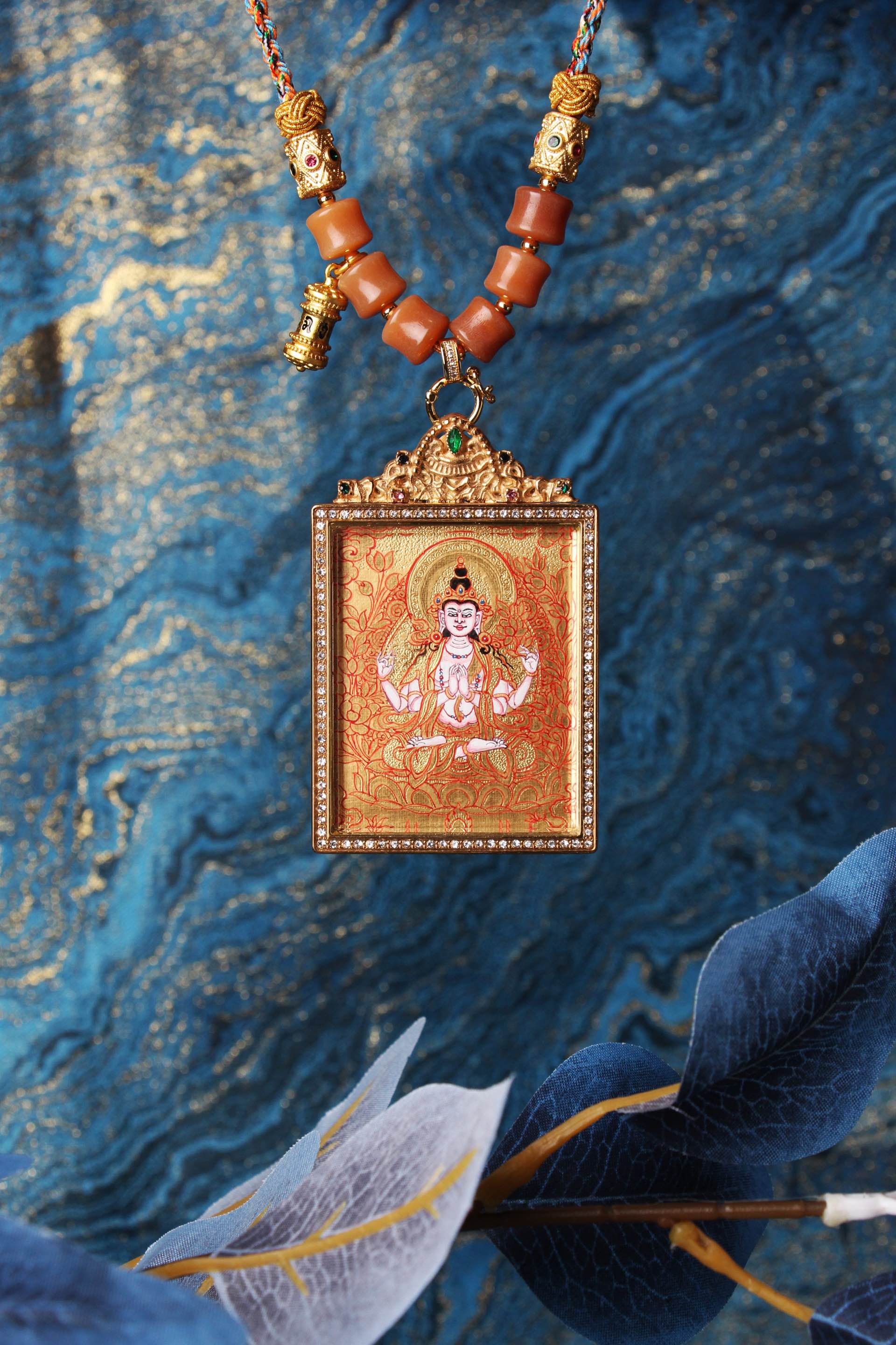 Close-up of a Rebgong-style Four-Armed Avalokiteshvara thangka pendant, highlighting the gold background, symmetrical four-arm iconography, jeweled frame, and traditional Tibetan craftsmanship.