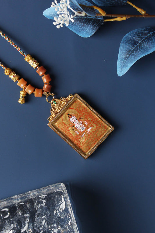 Angled view of Mahasthamaprapta mini thangka pendant showing fine gold thangka linework, layered mineral pigment texture, gemstone-accented titanium steel frame, and braided cord connection