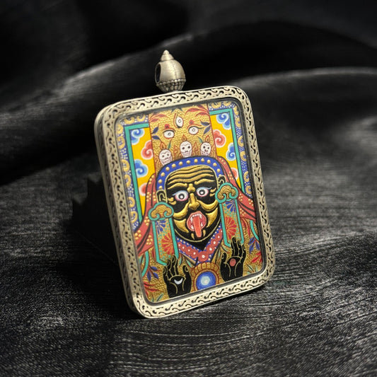 Angled view of Zaki Lhamo miniature thangka pendant highlighting raised gold powder facial detailing, vibrant traditional colors, and carved 925 silver frame.