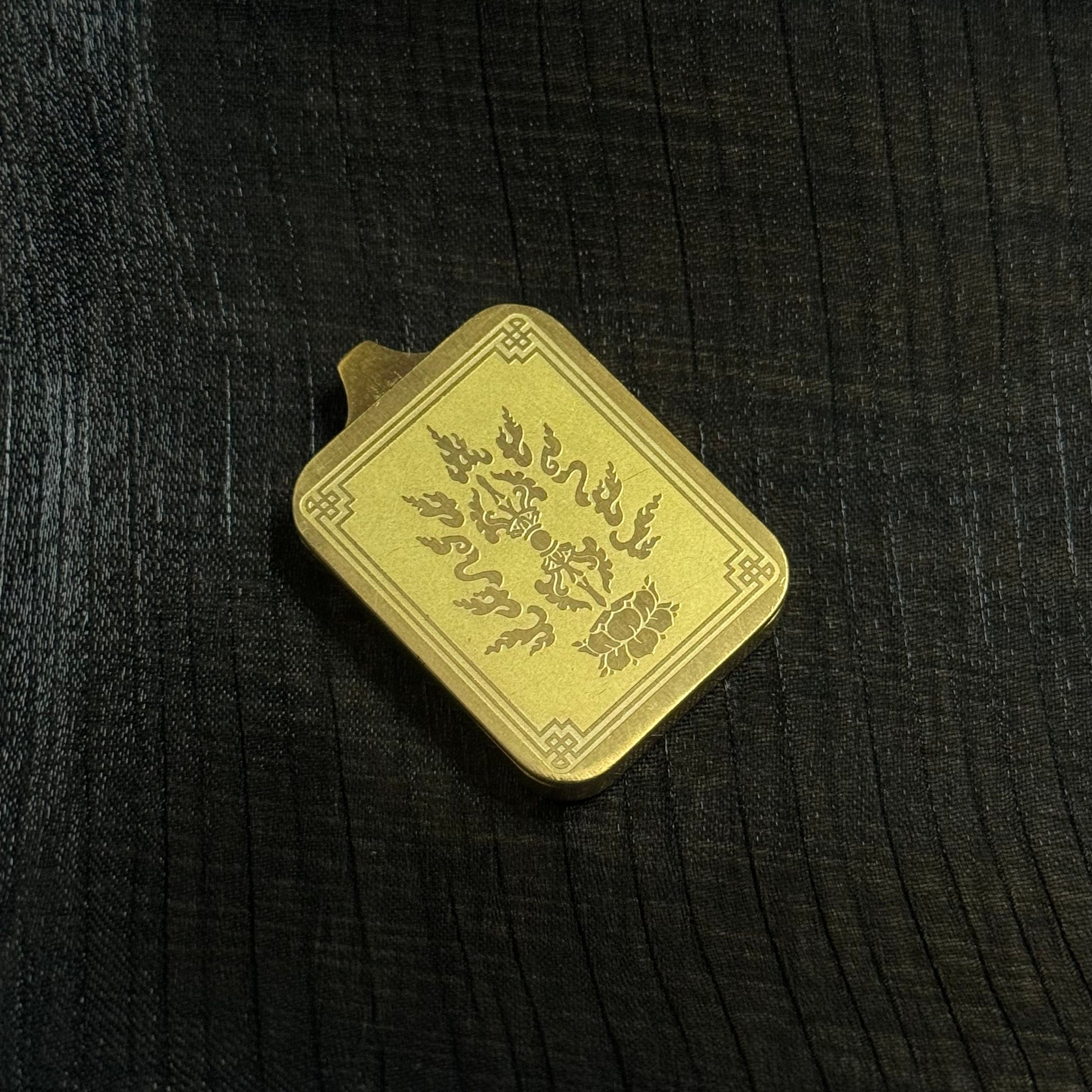 Back side of a Rebgong mini thangka pendant featuring engraved vajra and flame motifs on a gold-tone metal surface, representing traditional Tibetan Buddhist protective symbolism.