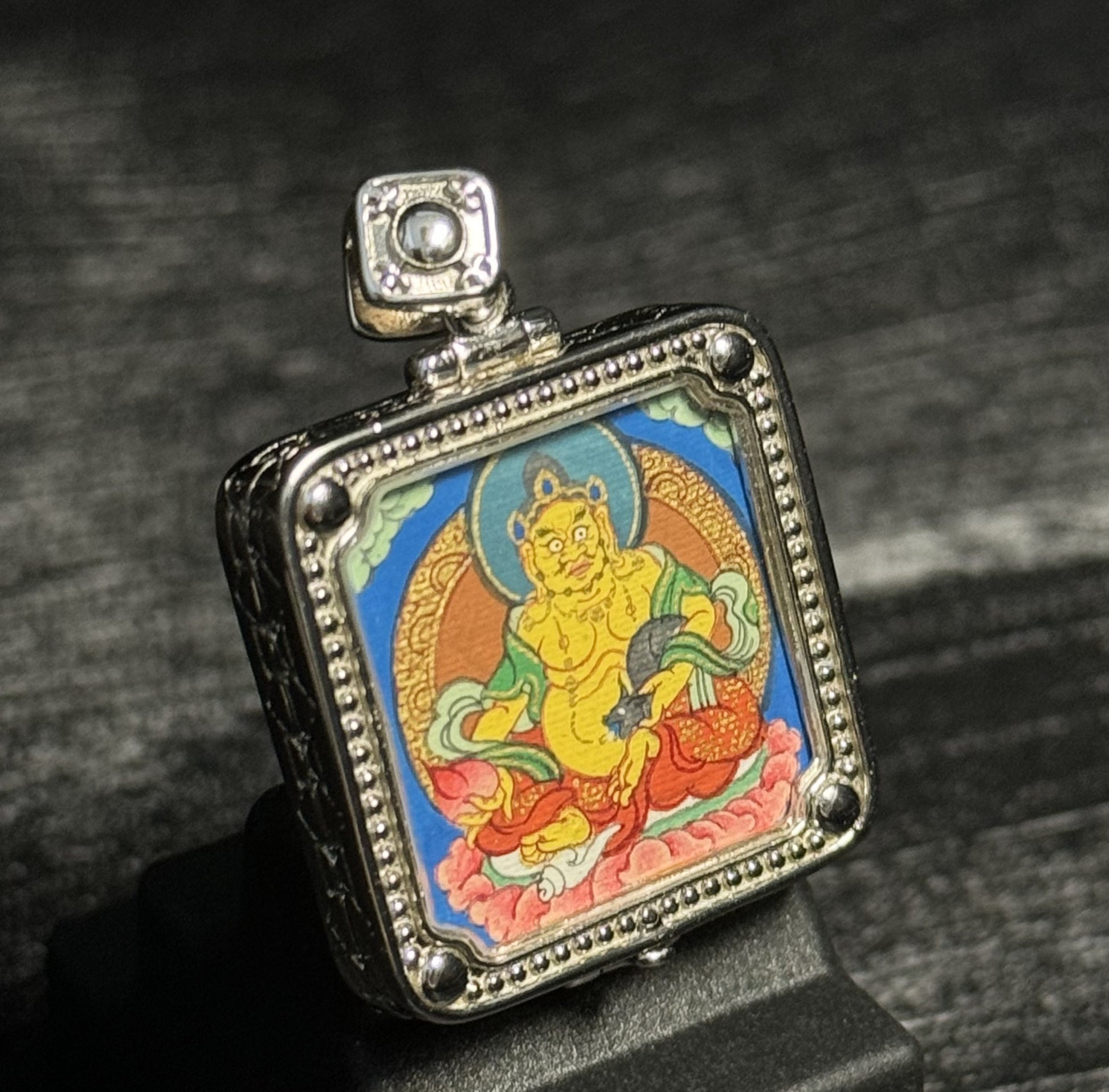Angled view of Rebgong Yellow Jambhala mini thangka pendant showing fine metal case details, hand-painted mineral pigments, designed for collection and inheritance