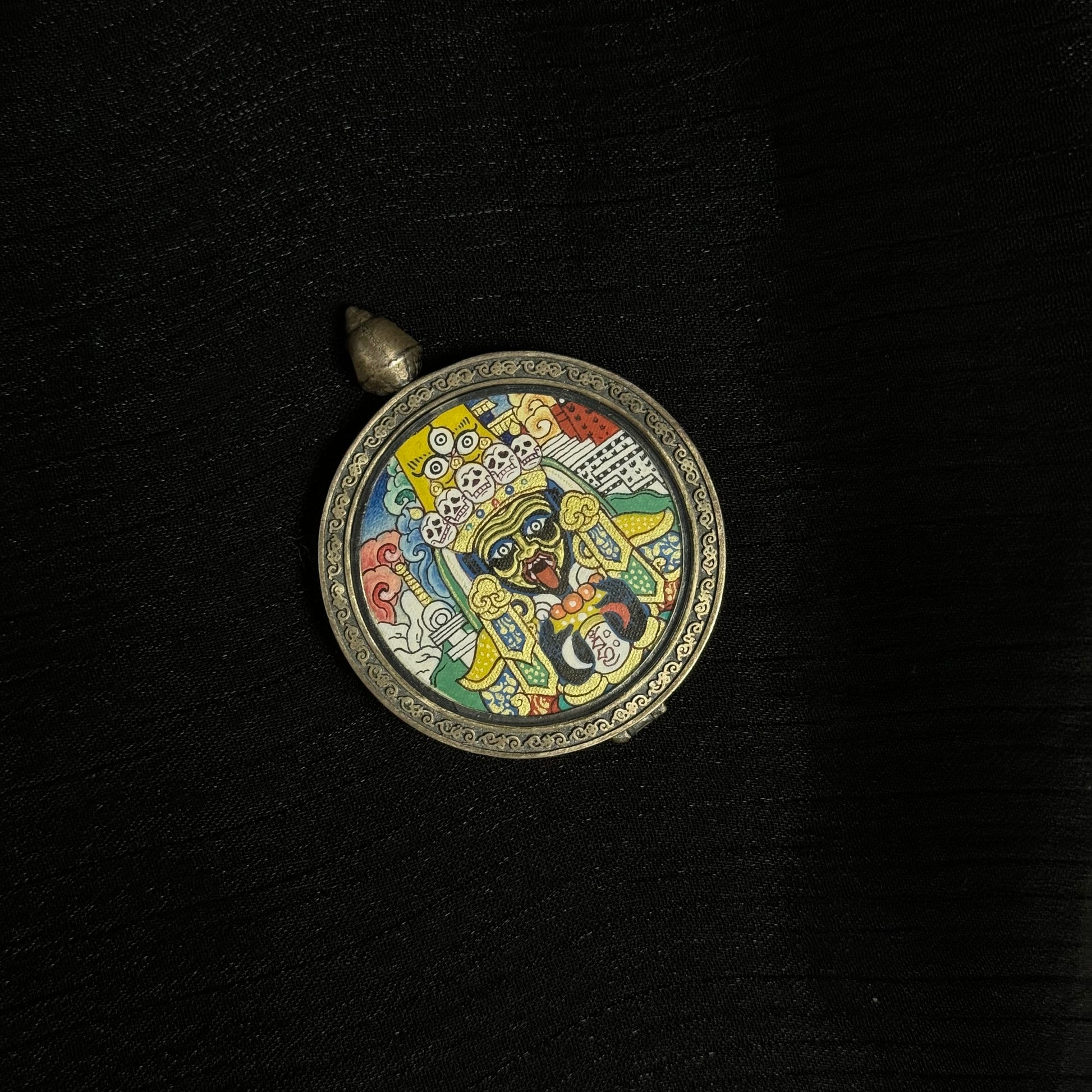 Top perspective of round Zaki Lhamo mini thangka pendant displaying the circular carved frame, pendant loop, and vibrant mineral pigment thangka painting.