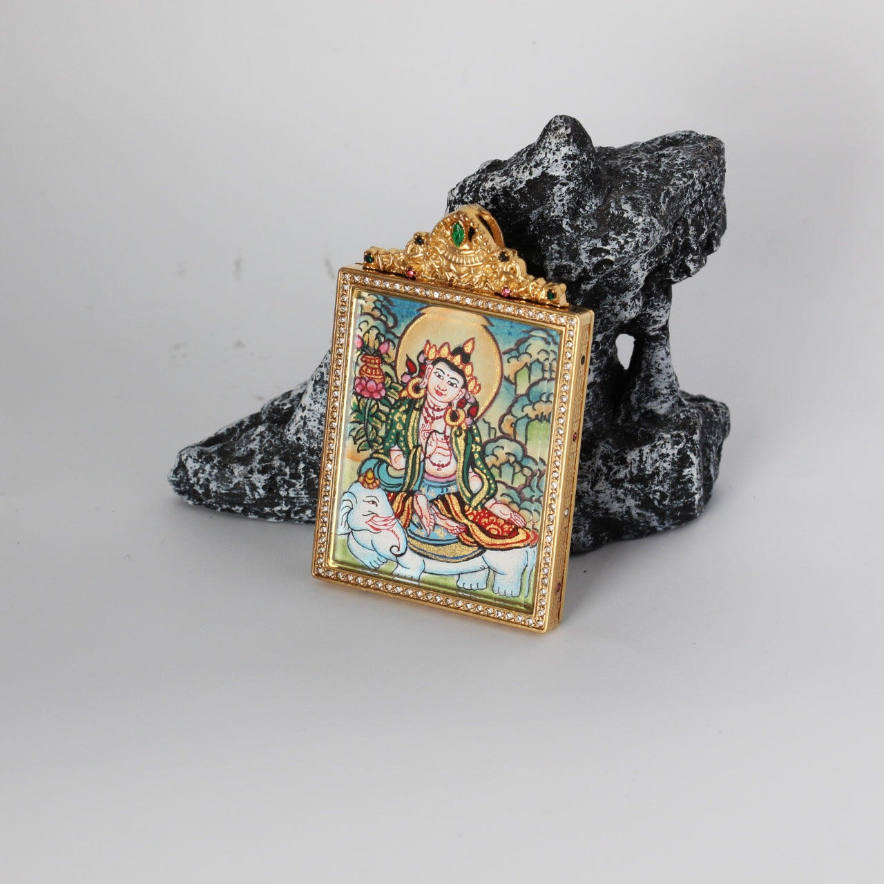 Angled view of the Samantabhadra Bodhisattva mini thangka pendant highlighting the crystal-set border, gold-tone titanium steel case depth, and the ornate crown top with green and multicolor stones, with the hand-painted elephant and bodhisattva artwork visible through the front window.