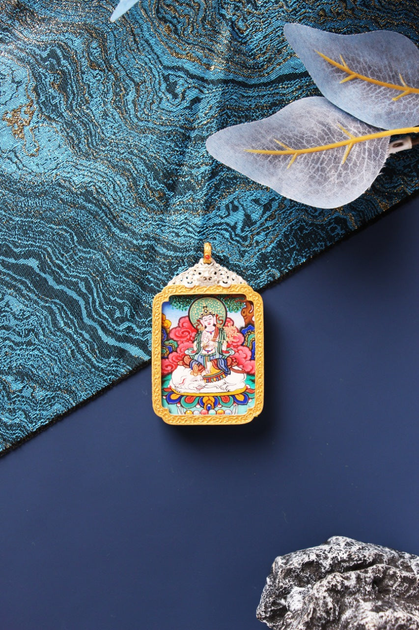 Front view of Samantabhadra Bodhisattva mini thangka pendant, showing the deity seated on a white elephant, richly colored mineral pigment painting, framed by a gold-tone border and ornate silver-plated top plate, styled on blue brocade fabric with translucent leaves and a dark stone accent.