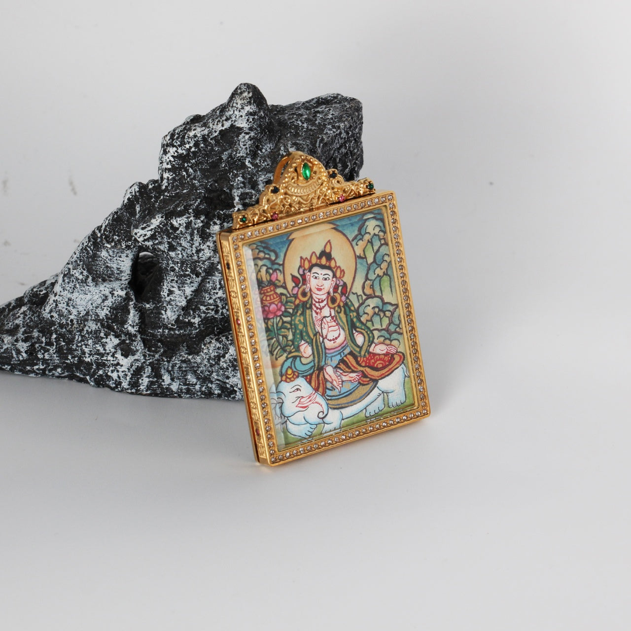 Side-angled photo of Samantabhadra Bodhisattva mini thangka pendant showing the gold-tone titanium steel case profile, crystal border around the front window, and the hand-painted Samantabhadra on white elephant image inside.