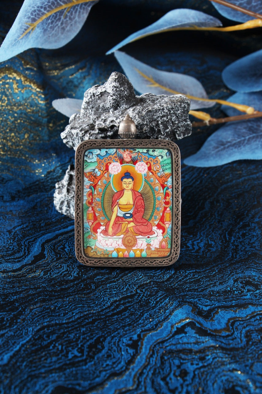 Front view of a Shakyamuni Buddha Menri mini thangka pendant, hand-painted with mineral pigments and set in a silver gawu-style case.