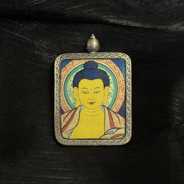 Angled view of Shakyamuni Buddha mini thangka pendant showing hand-painted Buddha portrait with mineral pigments inside a traditional silver pendant frame