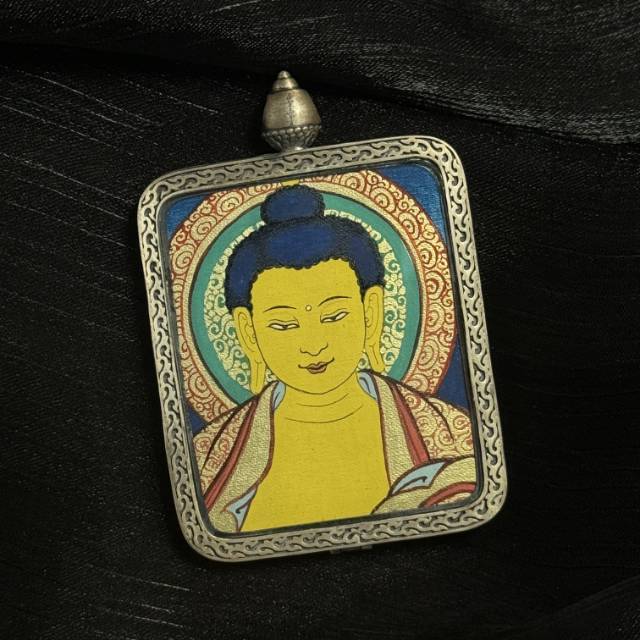 Close angled view of Shakyamuni Buddha mini thangka pendant highlighting detailed mineral pigment painting and decorative silver border