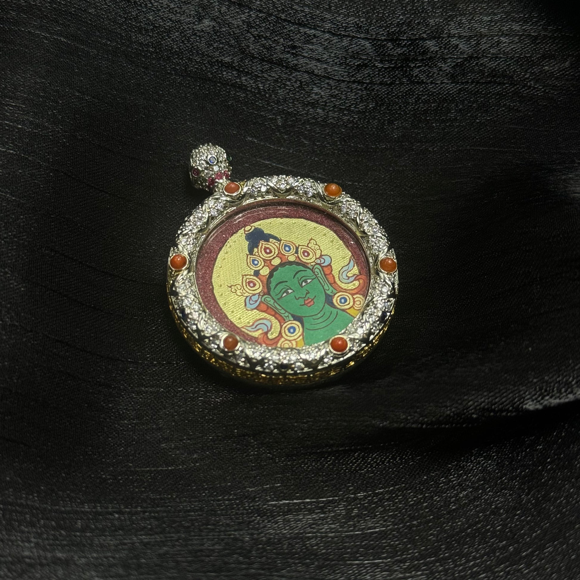 Side-angle view of a Green Tara hand-painted miniature thangka pendant with textured mineral pigment background and jeweled copper pendant frame featuring decorative gemstone inlays.