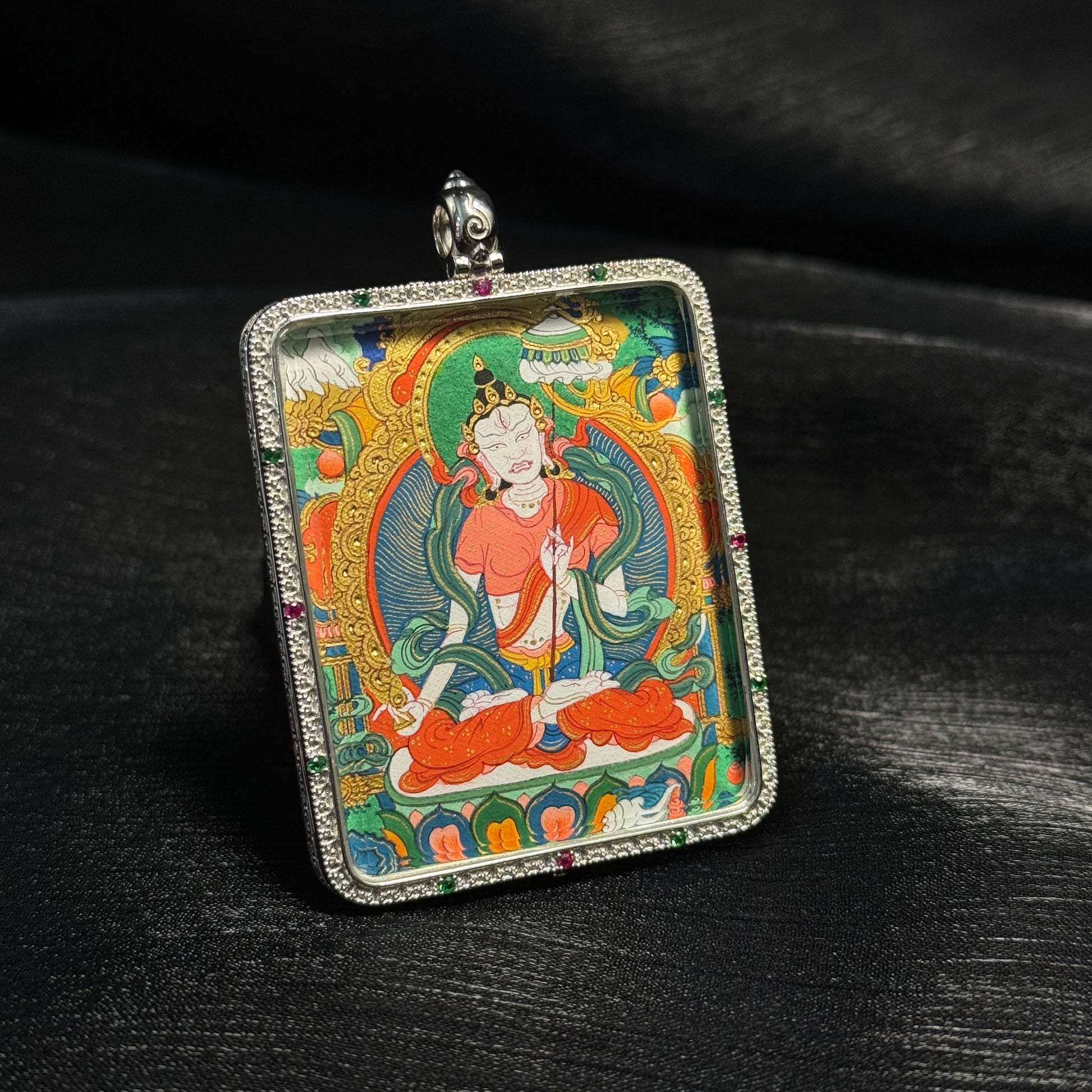 Angled view of Sitatapatra Tibetan mini thangka pendant showing detailed mineral pigment painting, gold powder highlights, and gemstone decorated silver frame.