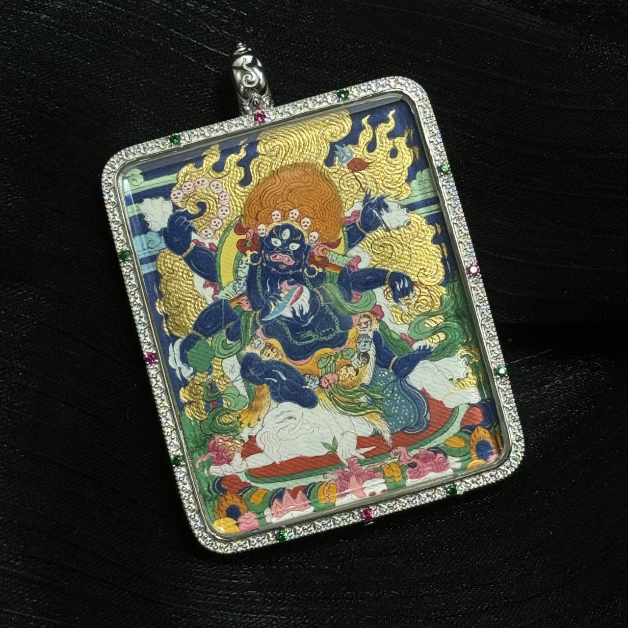 Detailed angled view of Six-Armed Mahakala thangka pendant showing layered mineral pigment painting and intricate silver pendant border