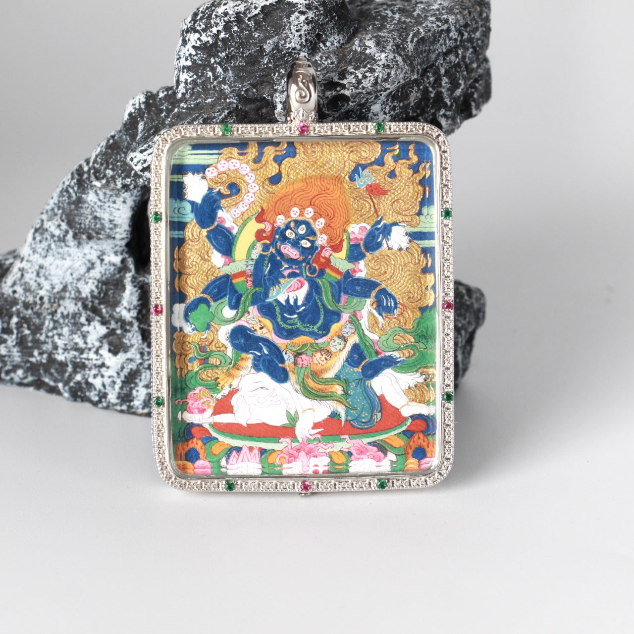 Close front view of the Six-Armed Mahakala thangka pendant showing fine hand-painted lines, layered mineral pigments, and the silver jewelry case with micro-set stones around the perimeter.