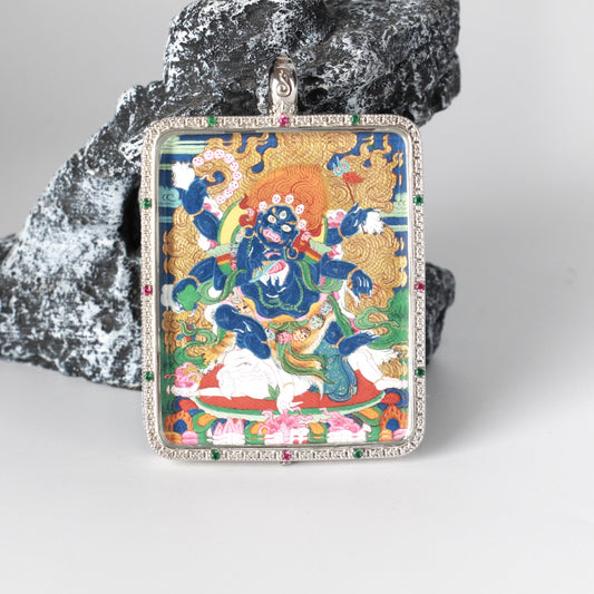 Close front view of the Six-Armed Mahakala thangka pendant showing fine hand-painted lines, layered mineral pigments, and the silver jewelry case with micro-set stones around the perimeter.