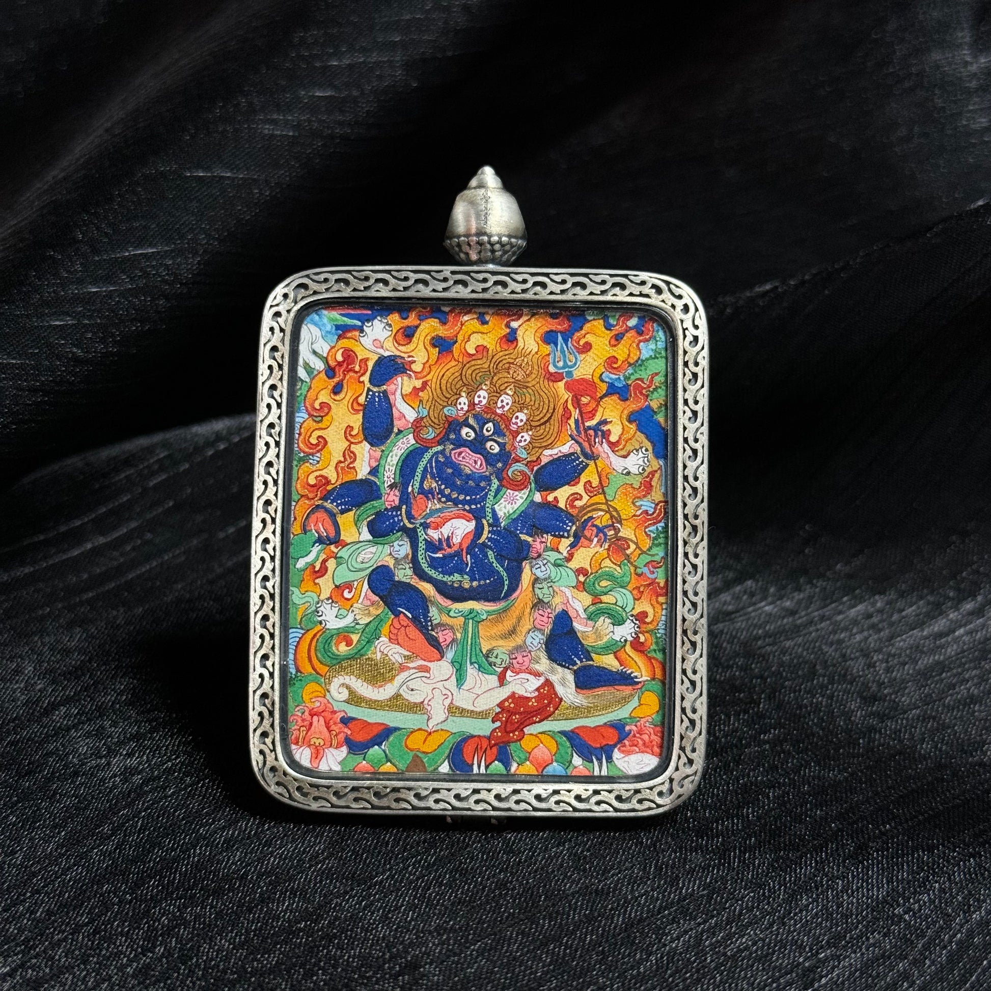 Front view of Six-Armed Mahakala mini thangka pendant, hand-painted with mineral pigments and gold powder, showing the fierce Tibetan protector deity within an ornate silver pendant frame