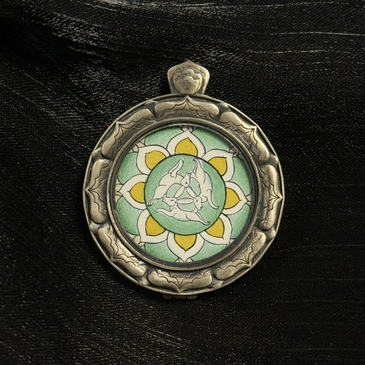Full view of round mini thangka pendant with three hares design, green and yellow color palette, 925 silver sculpted case, compact portable pendant format
