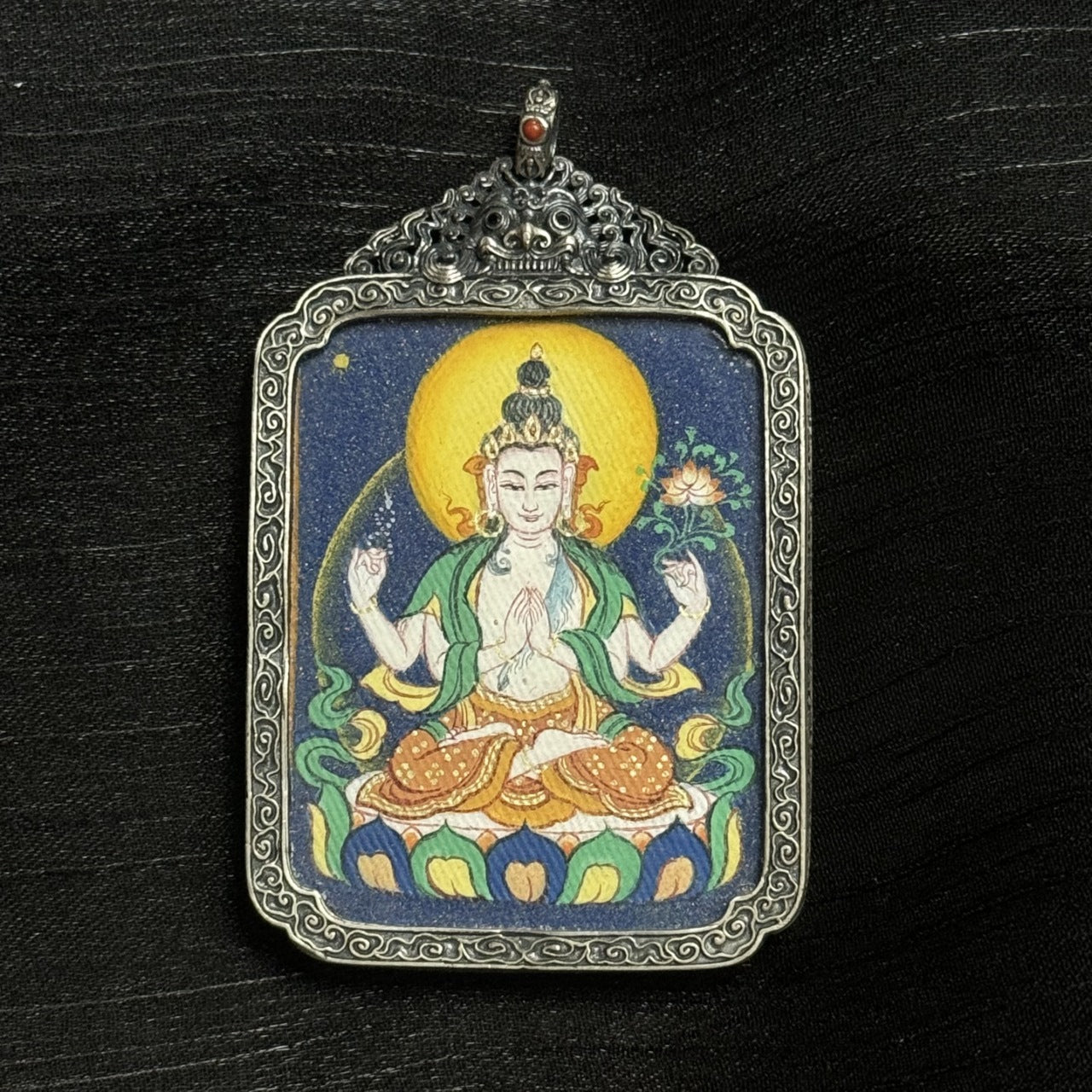 Full composition of Four-Armed Avalokiteshvara mini thangka pendant featuring deep blue background, circular aureole, balanced four-arm posture, and traditional Tibetan proportions.