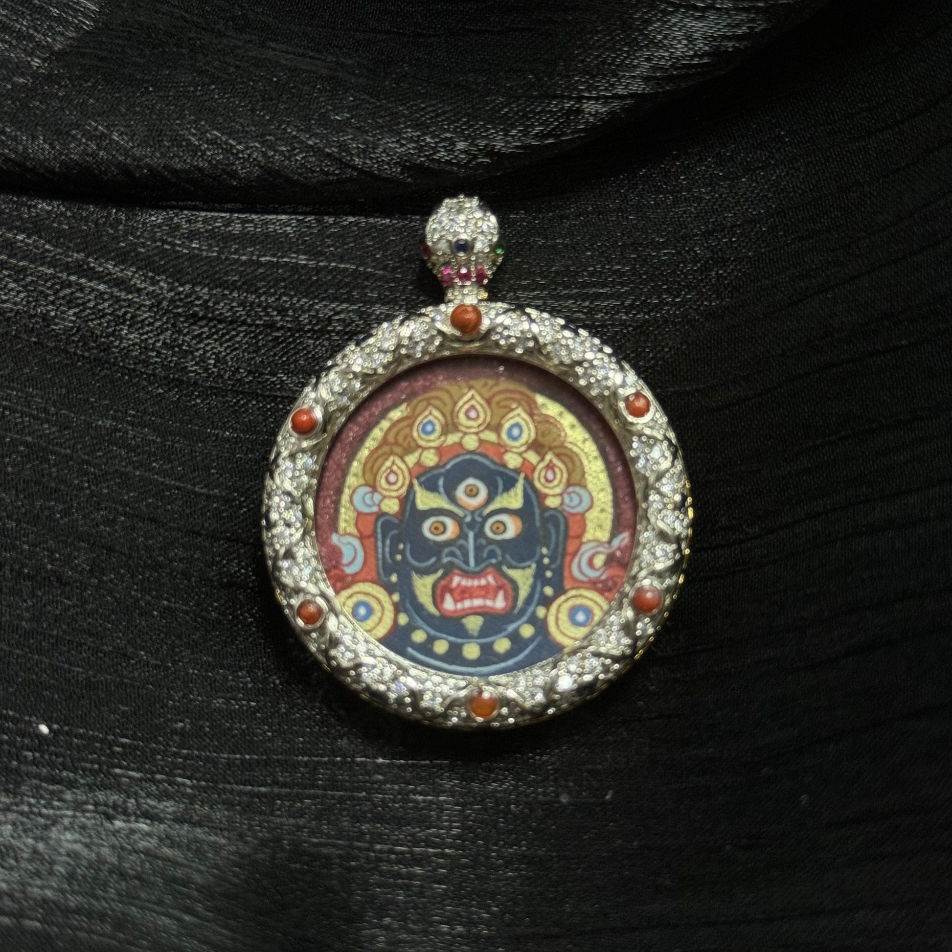 Round Tibetan thangka pendant depicting Acalanatha with cinnabar red background and gold halo, hand-painted Rebgong style