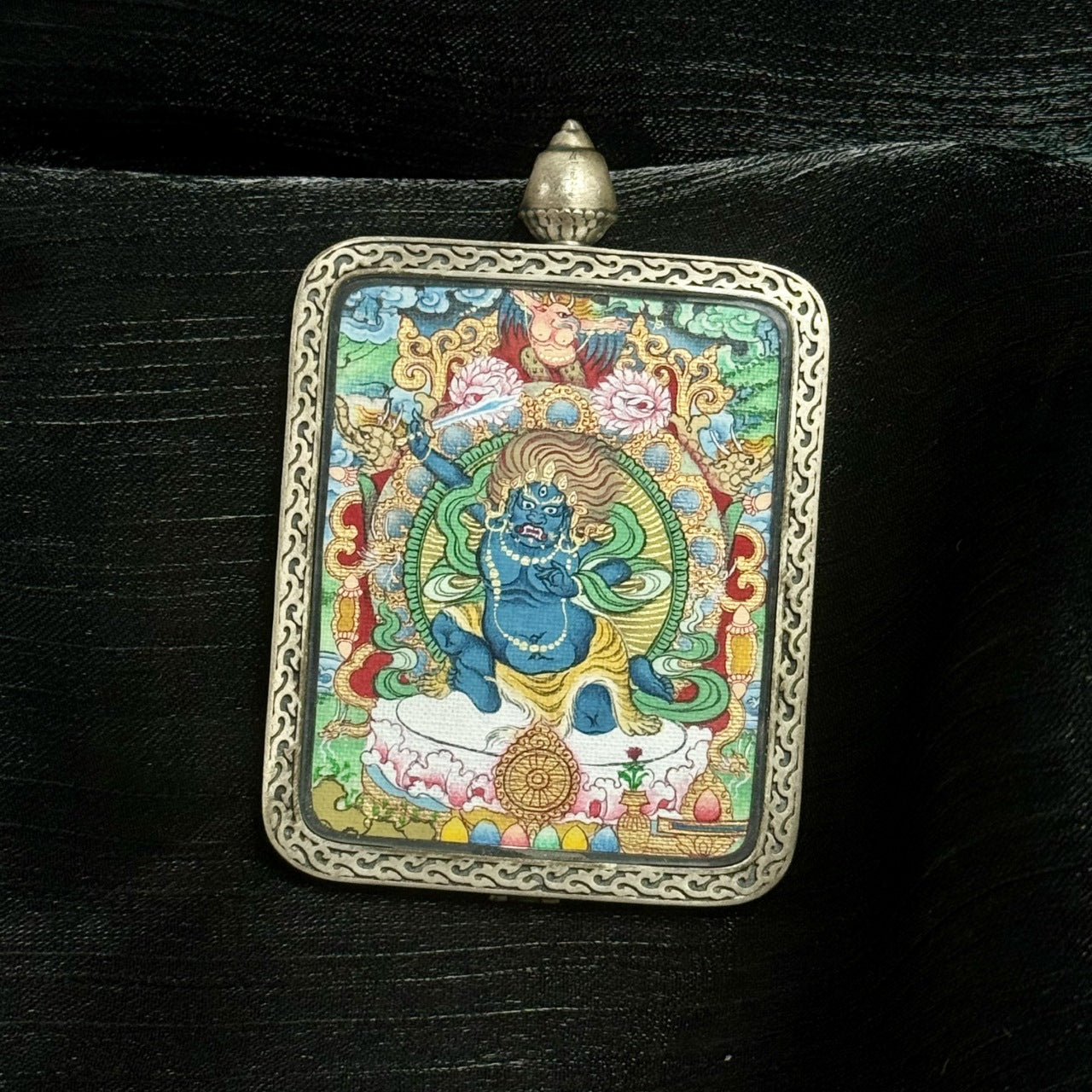 Full frontal composition of Acalanatha mini thangka pendant in a silver Dunhuang Nine-Color Deer case, displaying flame mandorla, fierce facial expression, ornamental lotus throne, and textured mineral pigment detailing.