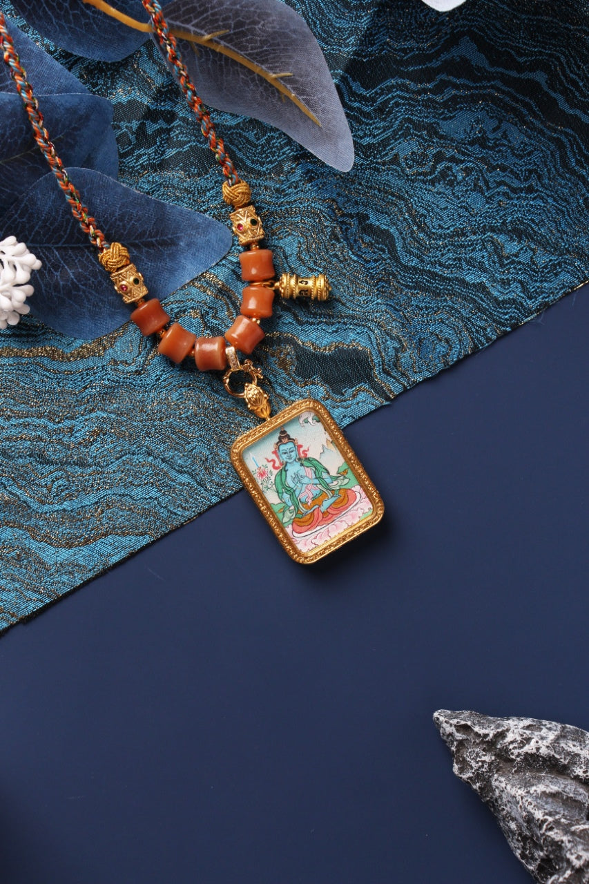 Tibetan Akashagarbha Bodhisattva mini thangka pendant displayed on textured fabric background, featuring a rectangular metal frame, fine painted lines, and necklace bead composition