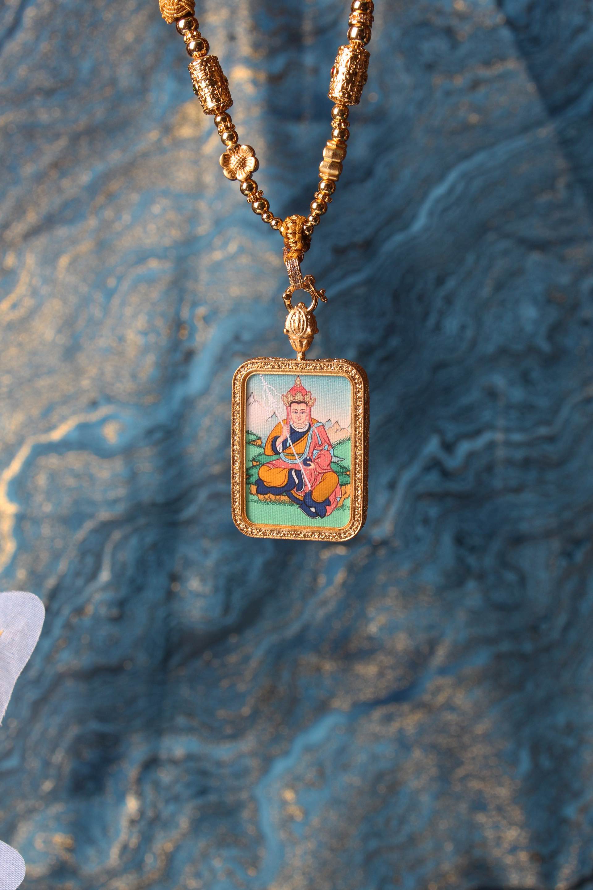 Ksitigarbha mini thangka pendant shown with gold-tone beads and frame, hand-painted mineral pigment artwork in Karma Gadri style