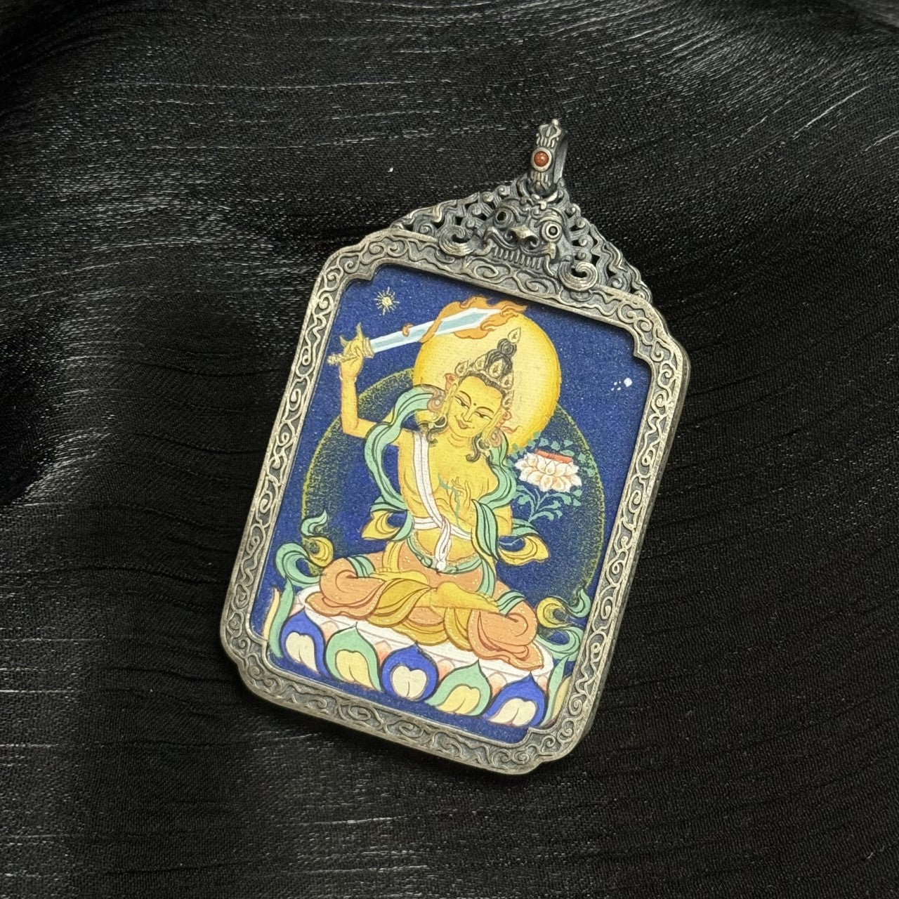 Front view of Manjushri Bodhisattva thangka pendant showing flaming wisdom sword, lotus base, golden halo, and layered mineral pigment texture.