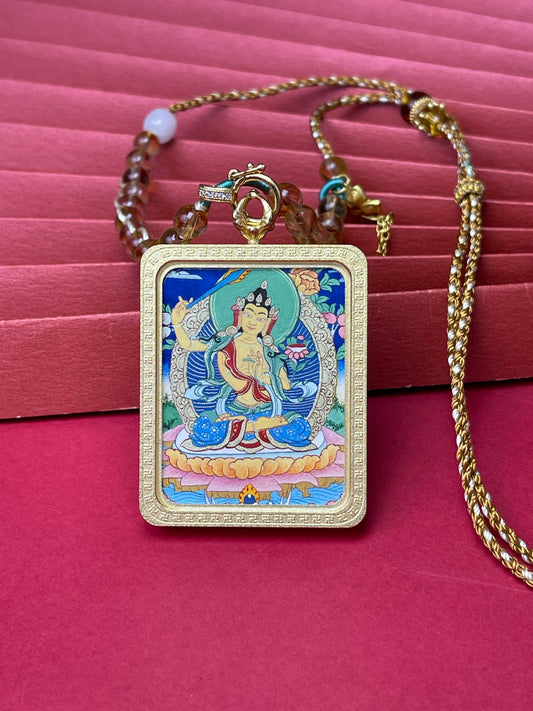 Close-up of Manjushri Bodhisattva thangka pendant showing hand-painted mineral pigment artwork inside a textured copper frame with yellow crystal woven necklace cord