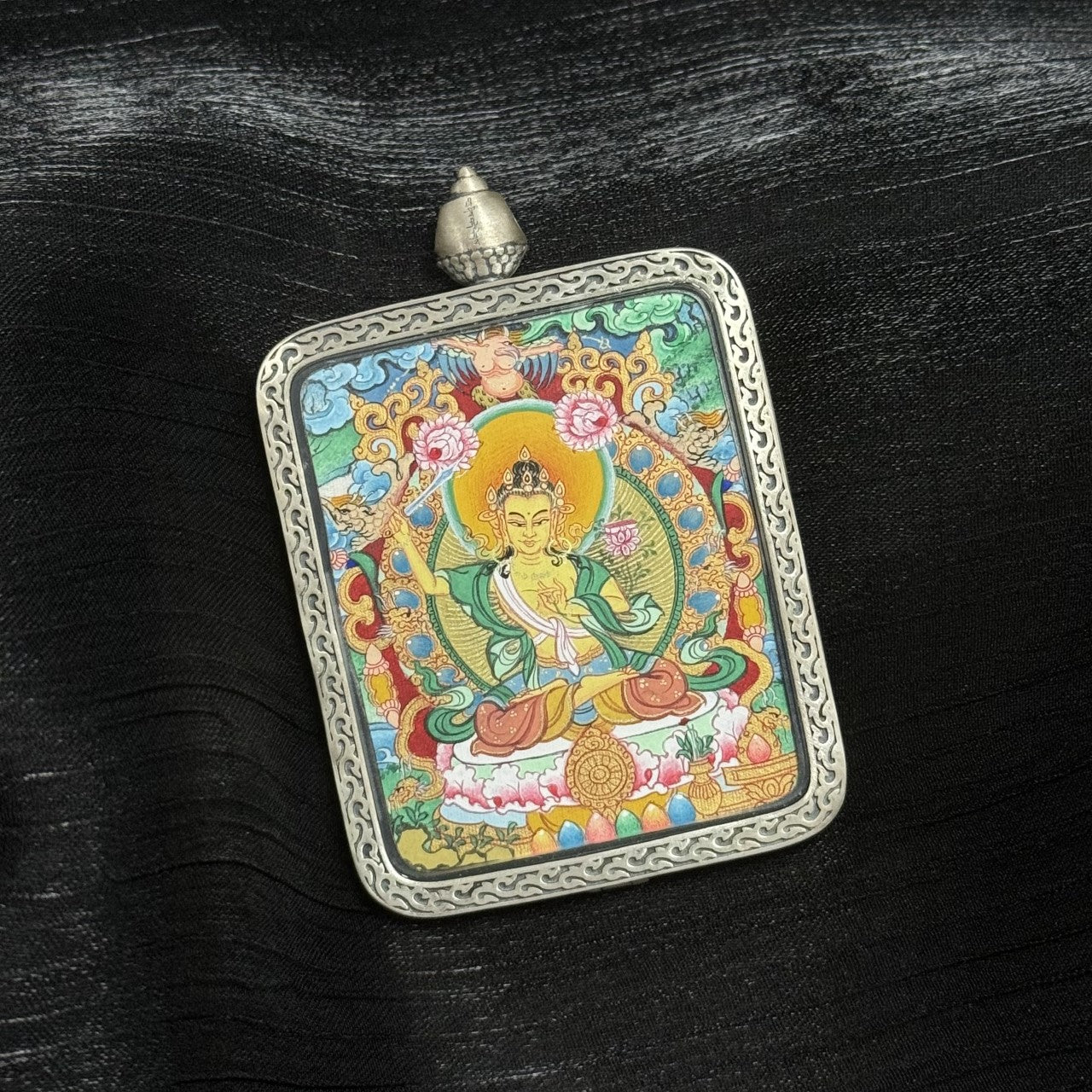 Close-up front view of Manjushri Bodhisattva mini thangka pendant highlighting facial detailing, sacred proportions, lotus throne base, offering motifs, and Dunhuang silver casing texture.