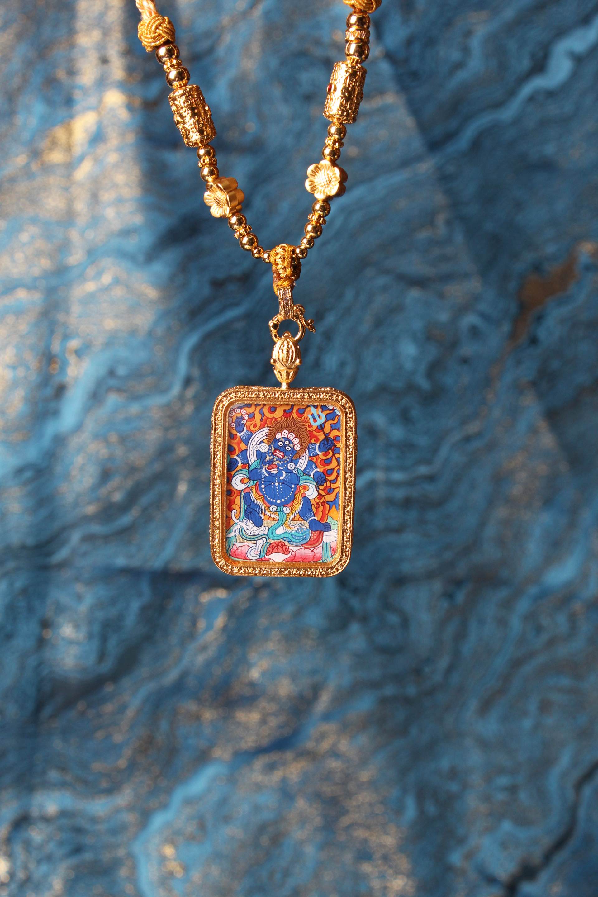 Six-Armed Mahakala mini thangka pendant in Rebgong Tibetan style, shown with gold-tone beads, hand-painted mineral pigment artwork, and decorative background