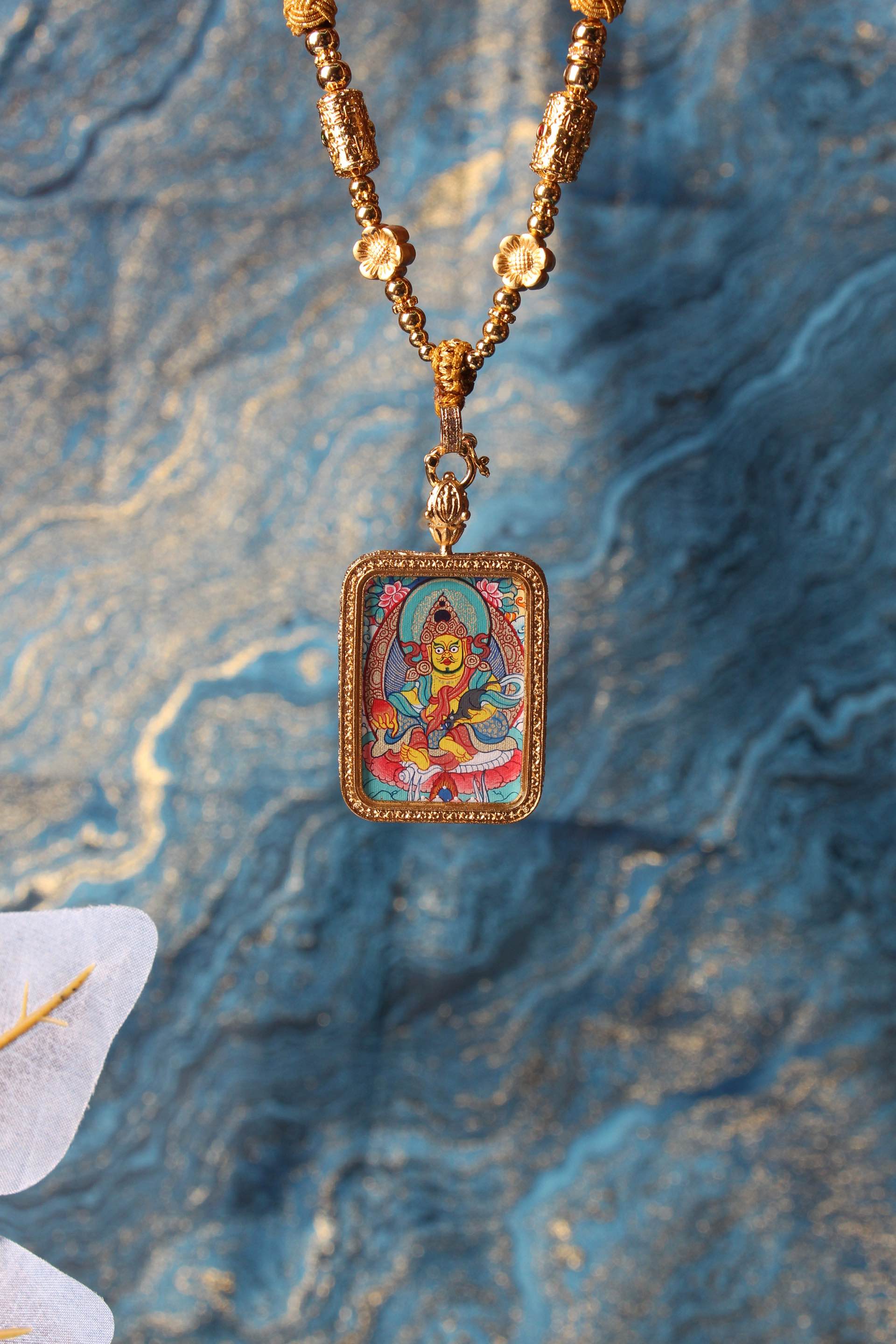 Yellow Jambhala mini thangka pendant shown with gold-tone beads and frame, hand-painted mineral pigment artwork against decorative background
