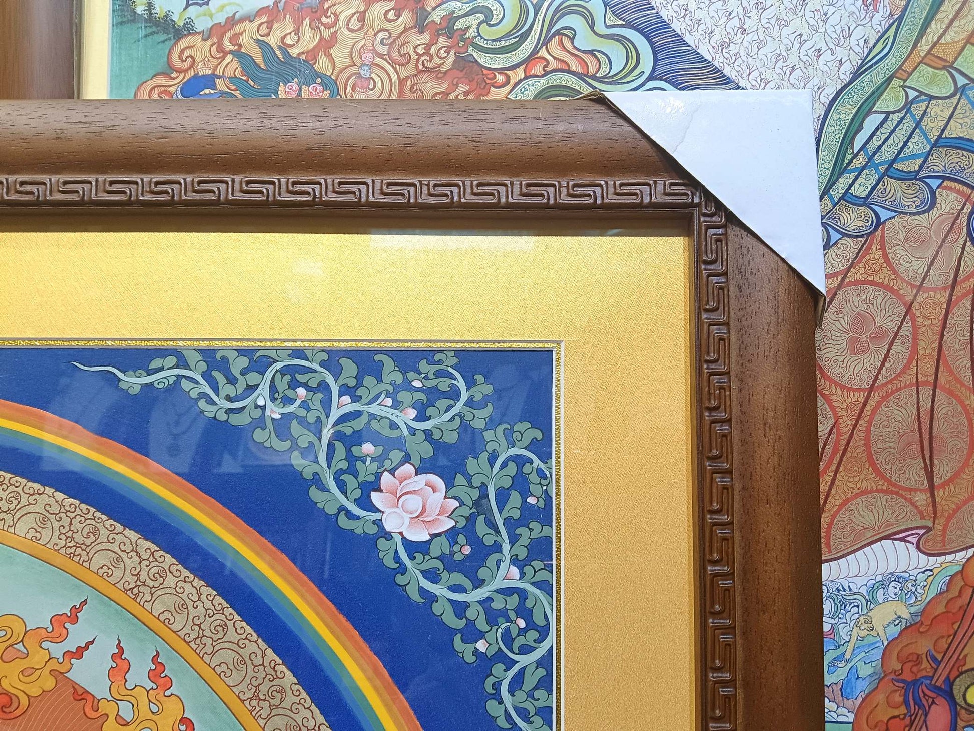Detail of the solid wooden frame and decorative border of a large Tibetan thangka featuring floral motifs and vibrant mineral pigment colors.