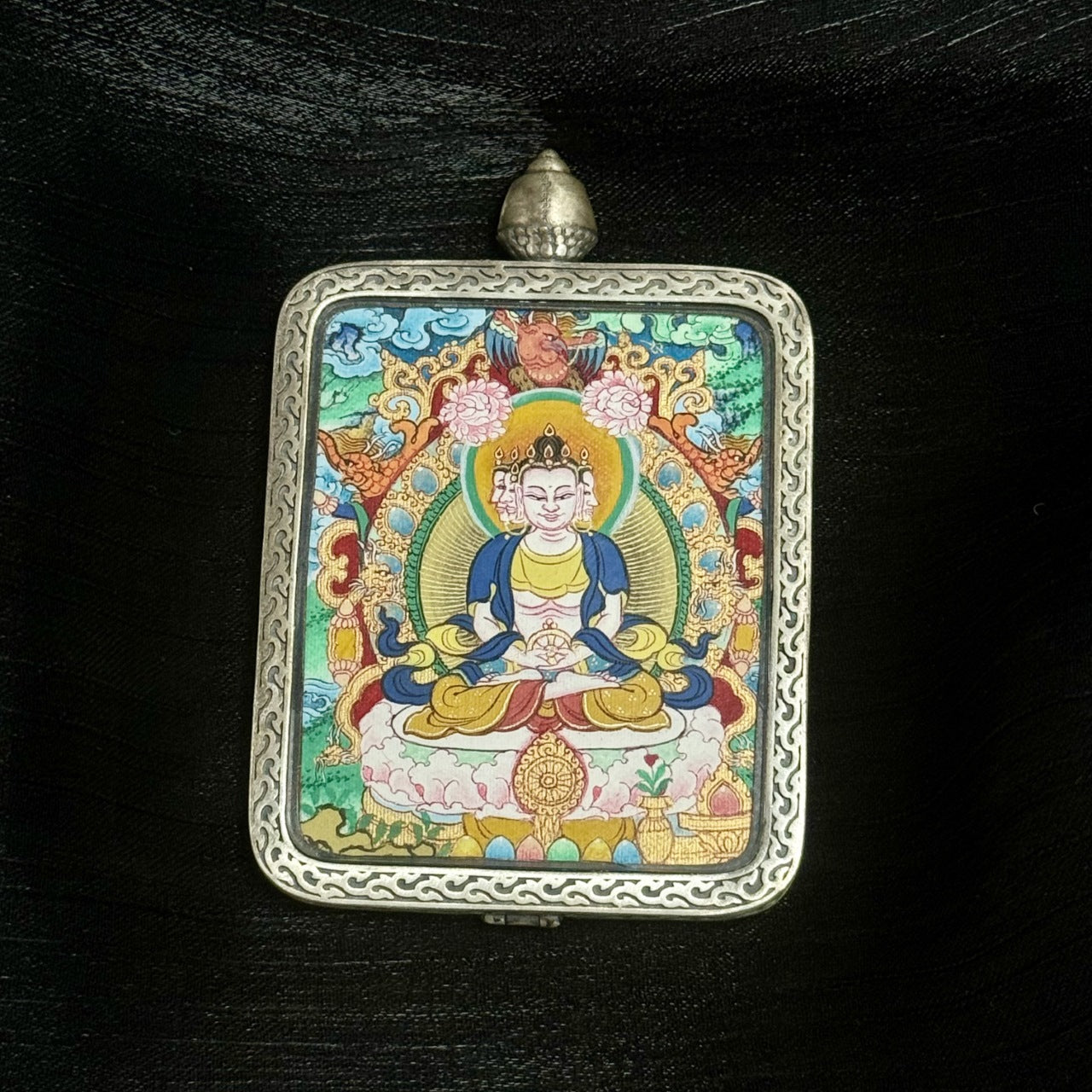 Centered full-frame image of Vairocana Buddha portable thangka pendant, Tibetan origin, mineral pigment painting inside decorative silver frame.