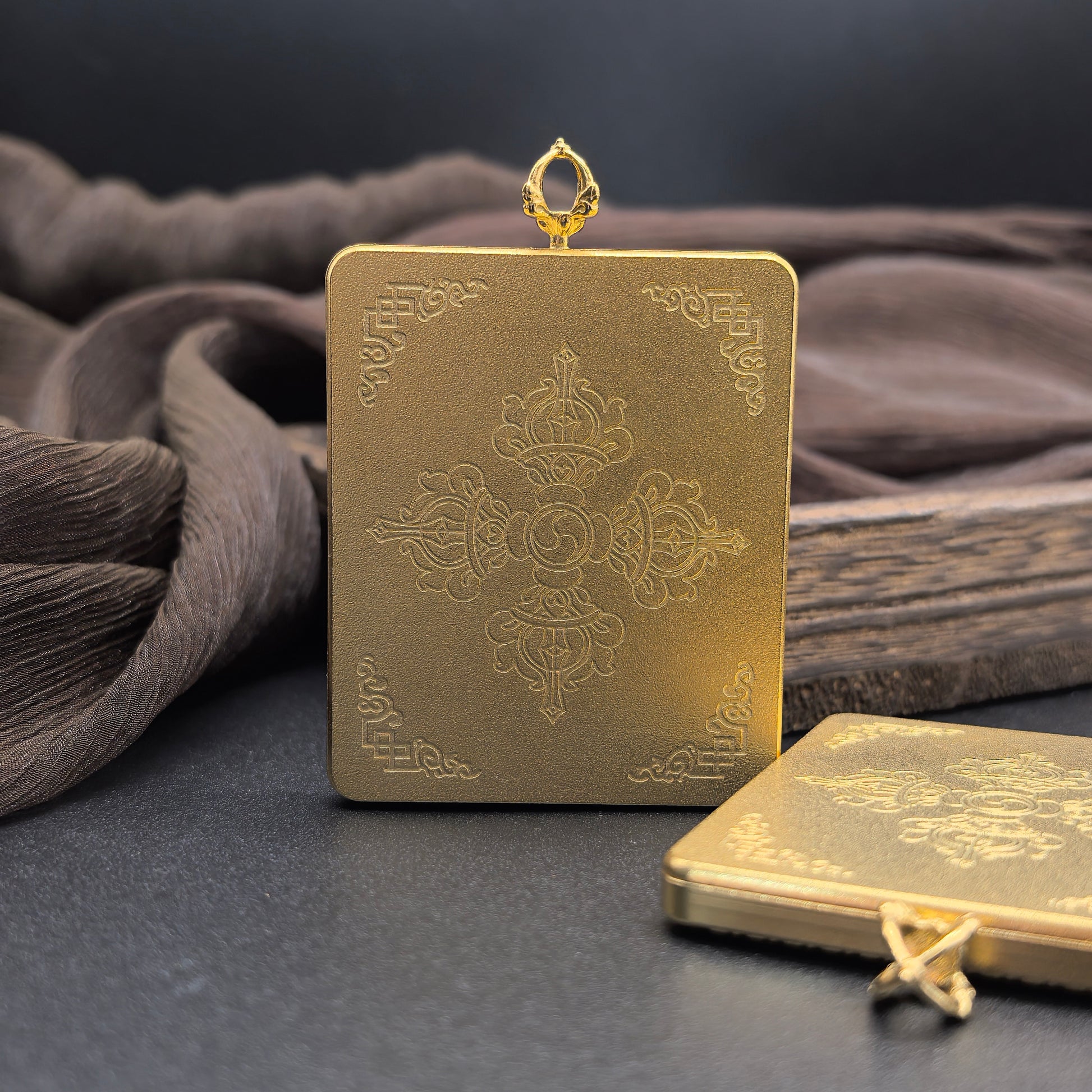 Back view of mini thangka pendant showing engraved Vajrayana cross symbol on the gold-colored protective case with Tibetan decorative patterns.