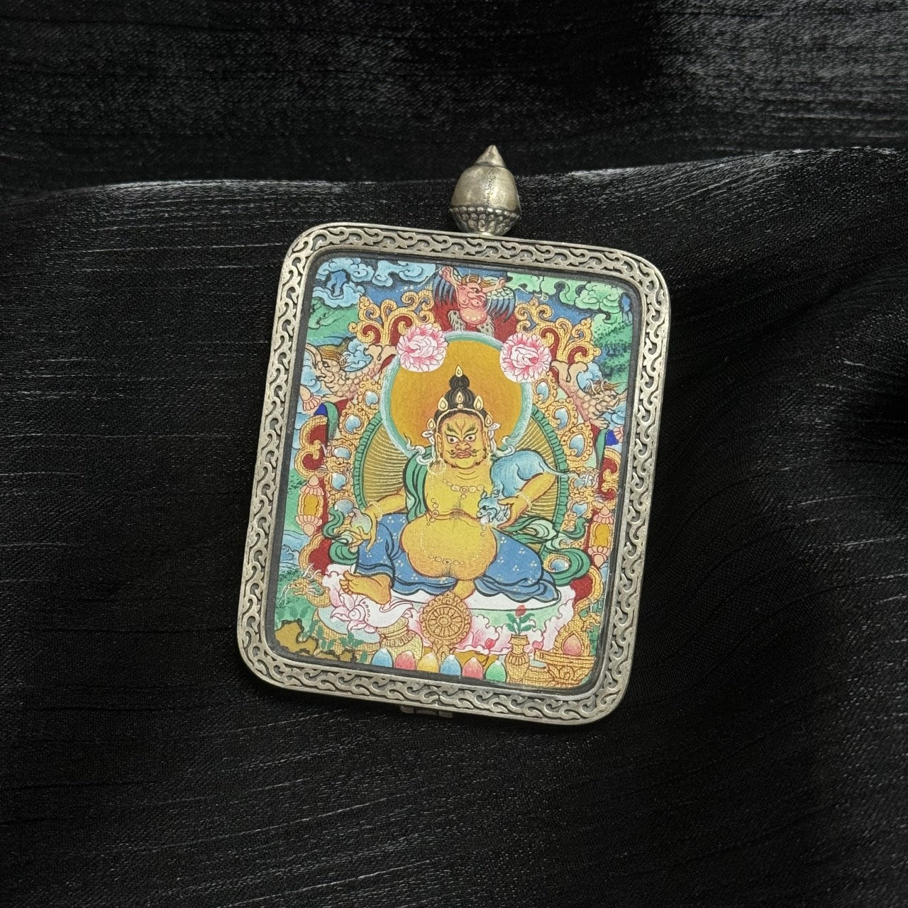 Close-up of Tibetan Yellow Jambhala hand-painted miniature thangka pendant highlighting intricate linework, symmetrical composition, vibrant mineral colors, and traditional Tibetan proportional design.