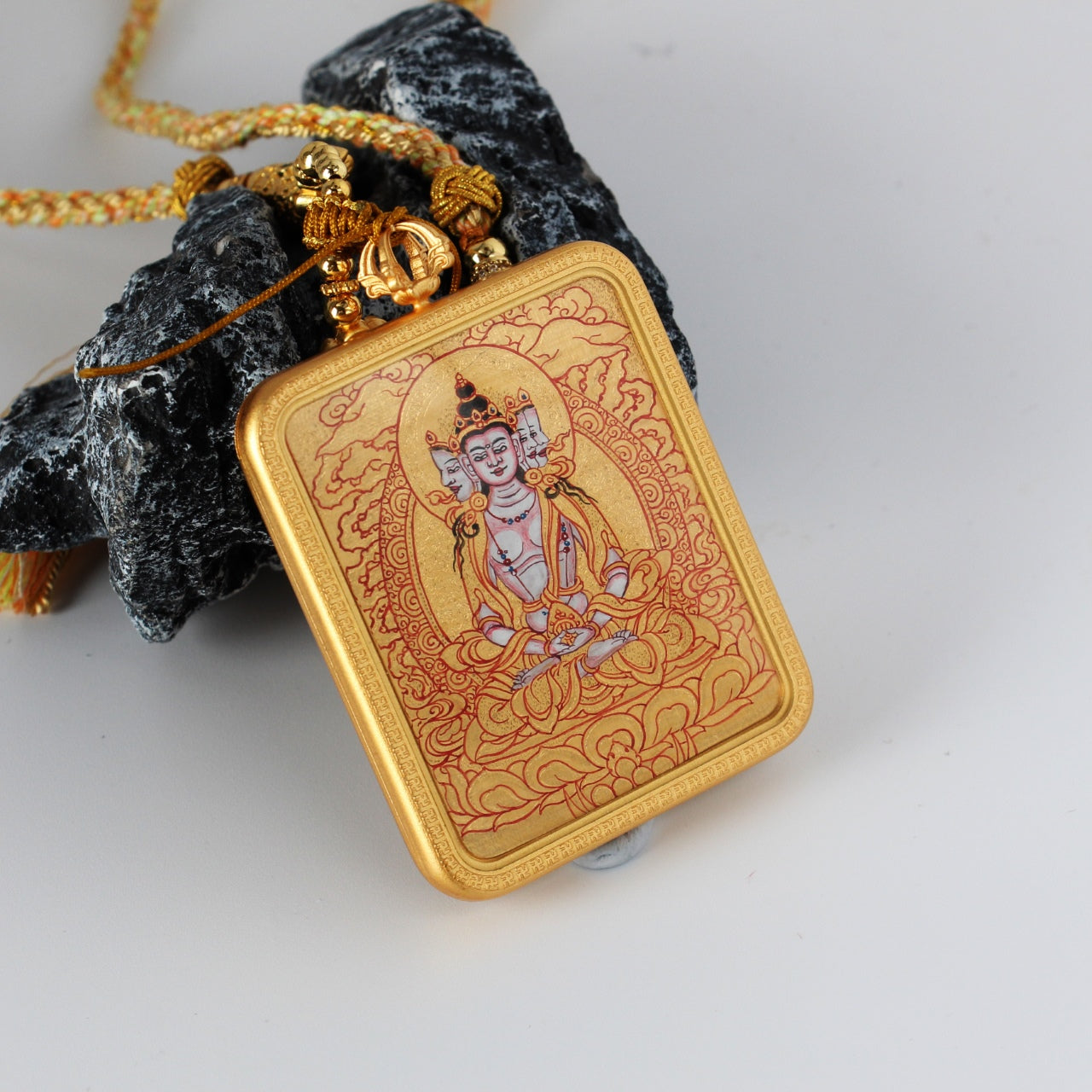 Angled close-up of a Vairocana Buddha mini thangka pendant highlighting layered mineral pigments, fine line work, and traditional Rebgong gold thangka painting techniques.