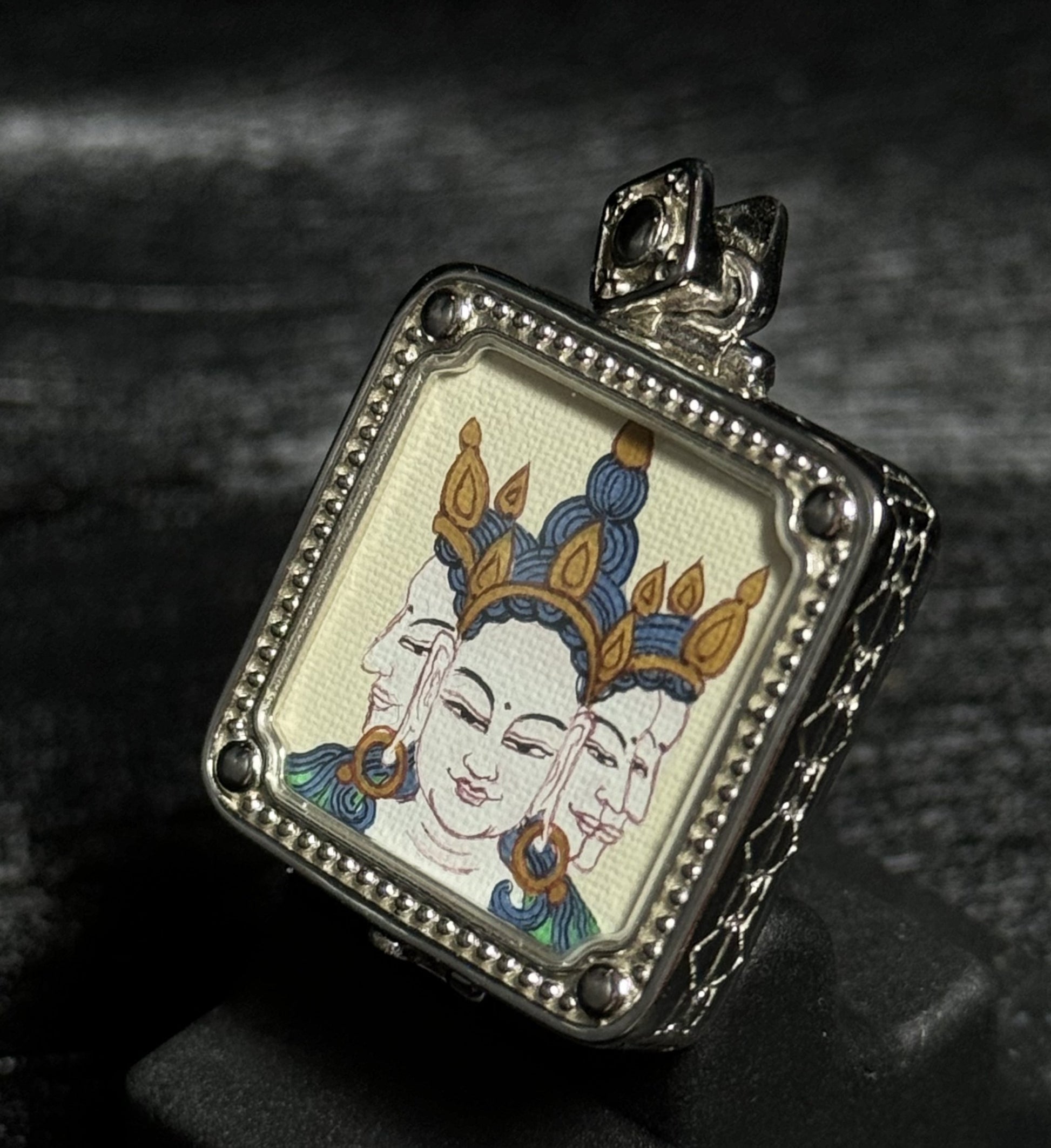 Close-up detail of the Vairocana Buddha portrait in a miniature thangka pendant, showing the three-faced Buddha painting and silver framed setting.