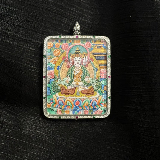 Close-up front view of the Vairocana Buddha mini thangka pendant featuring the serene Buddha seated on a lotus throne surrounded by colorful floral motifs and traditional Tibetan decorative elements within a silver pendant frame.