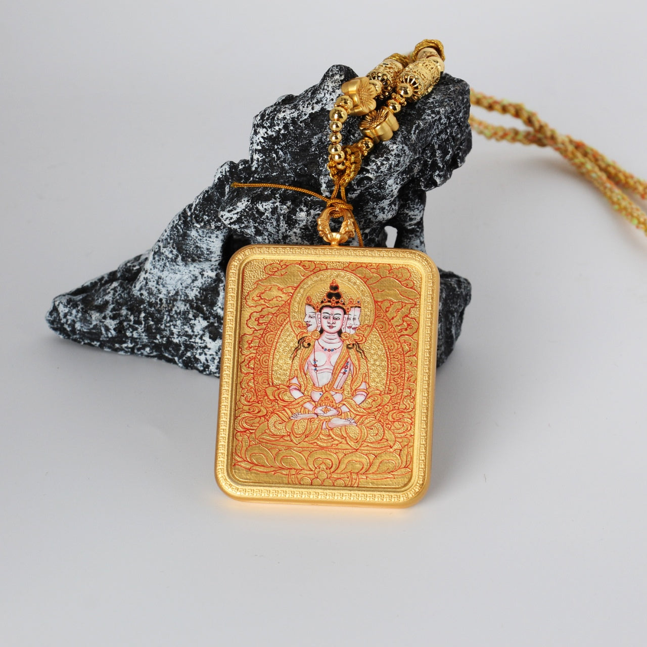 Front view of a Vairocana Buddha mini thangka pendant, fully hand-painted with mineral pigments in Rebgong gold thangka style, set in a copper case with intricate red and gold detailing.